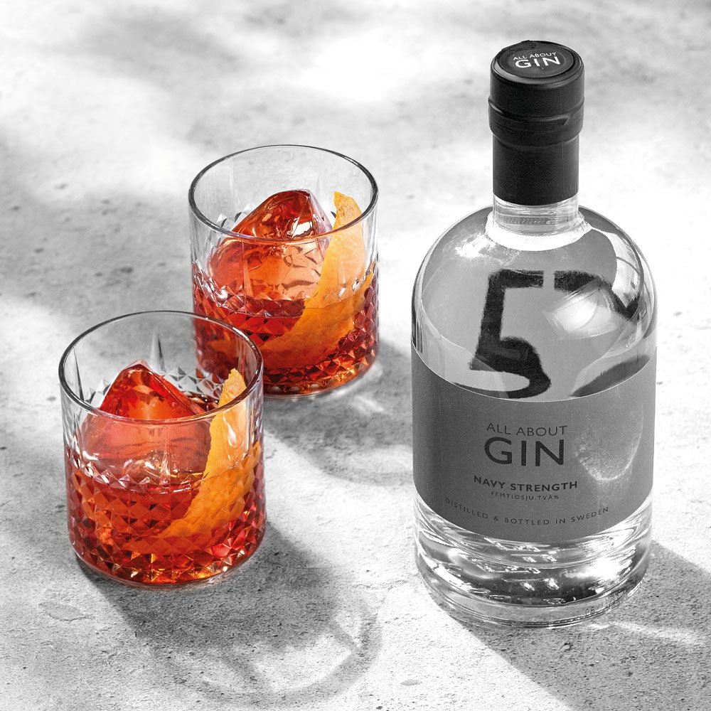Negroni cocktail med apelsin och ginflaska mot grå bakgrund.