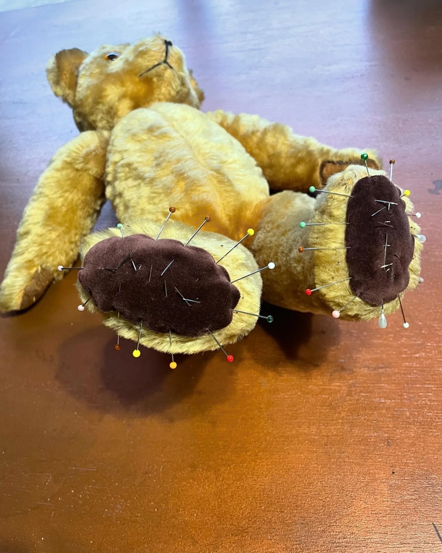 Teddy bear being restored with pins in its feet  and new felt pads.