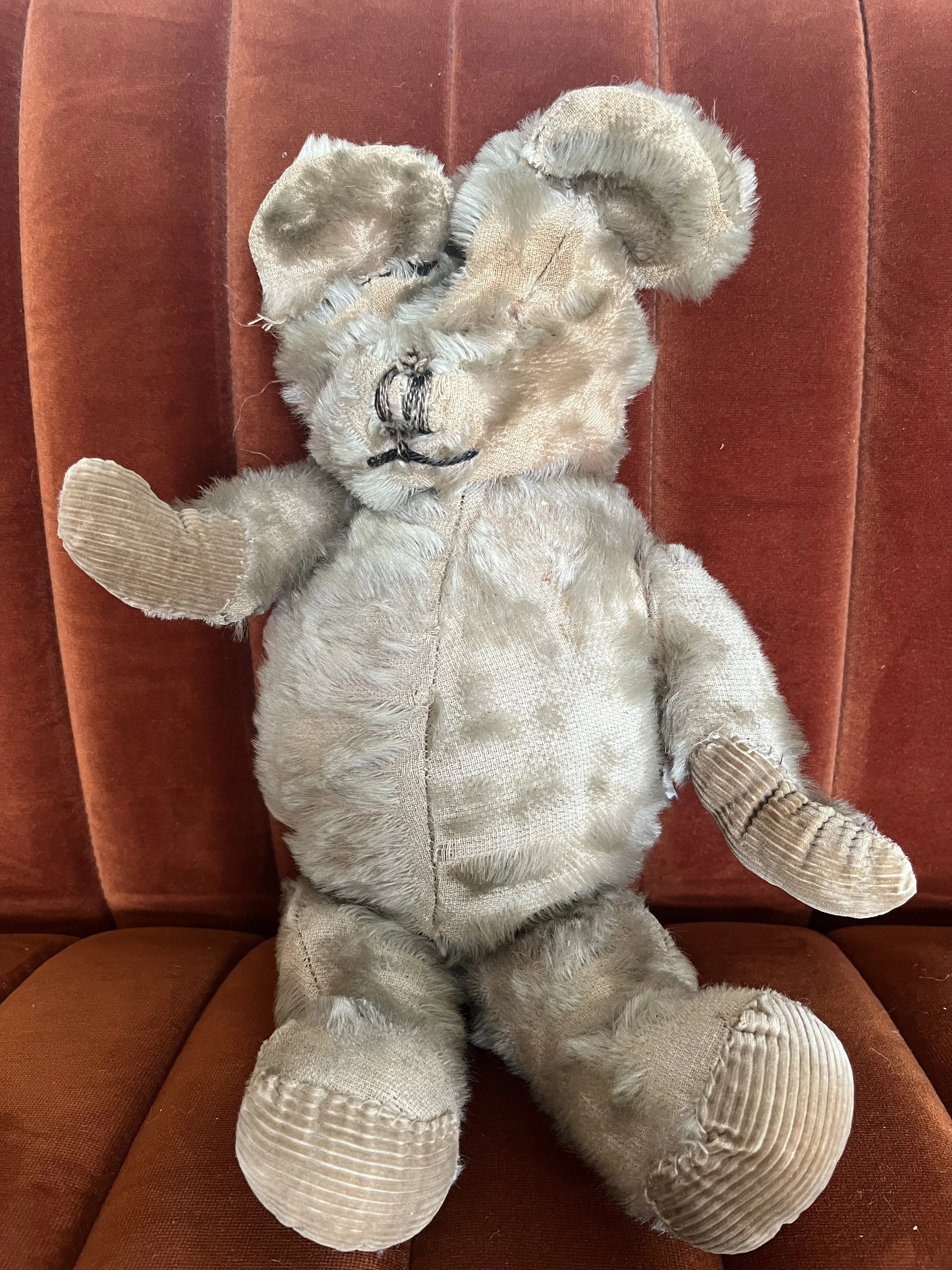 Vintage teddy bear with worn fur sitting on a brown couch
