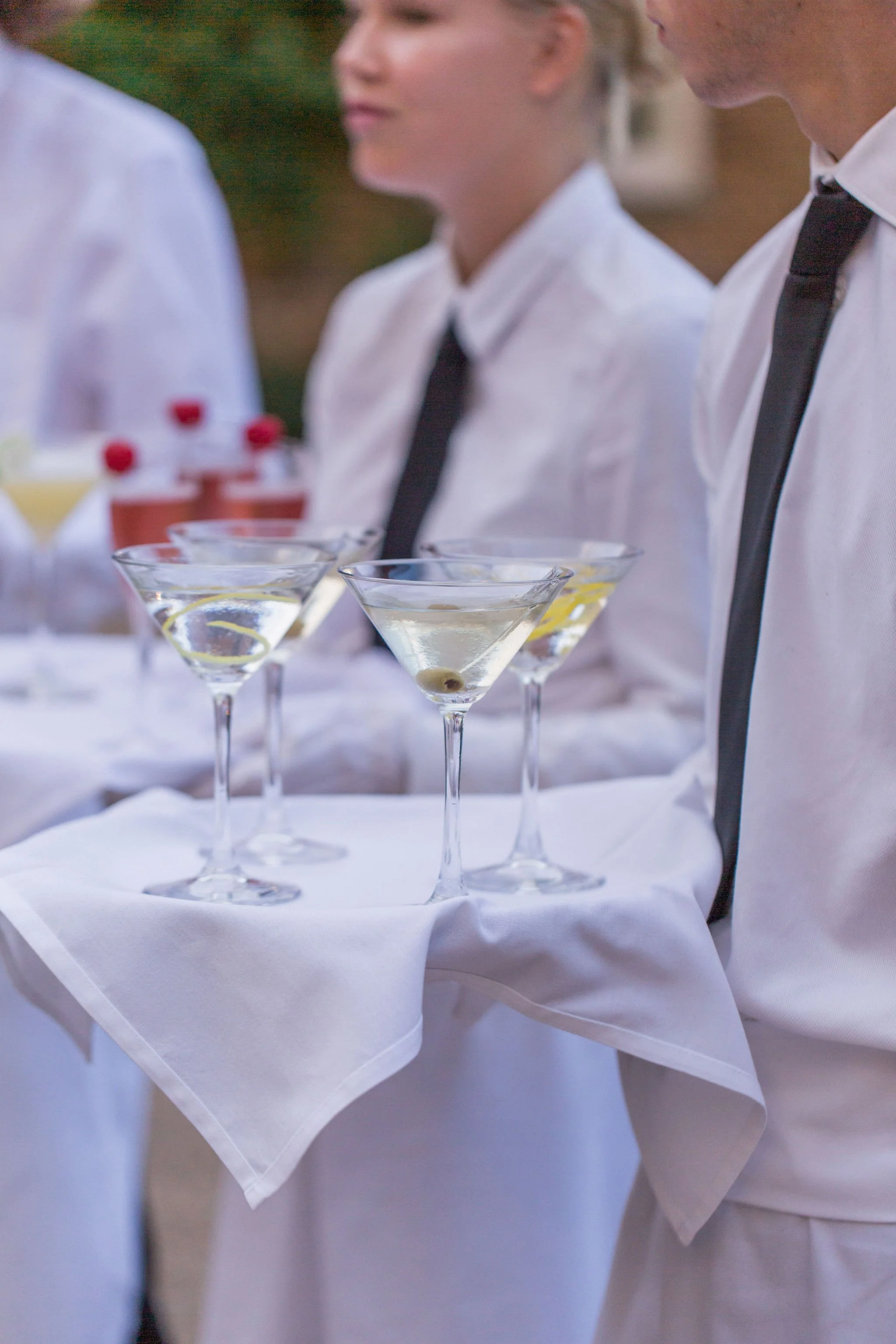Waitstaff serving cocktails at an outdoor event, with people dressed in white shirts and black ties.