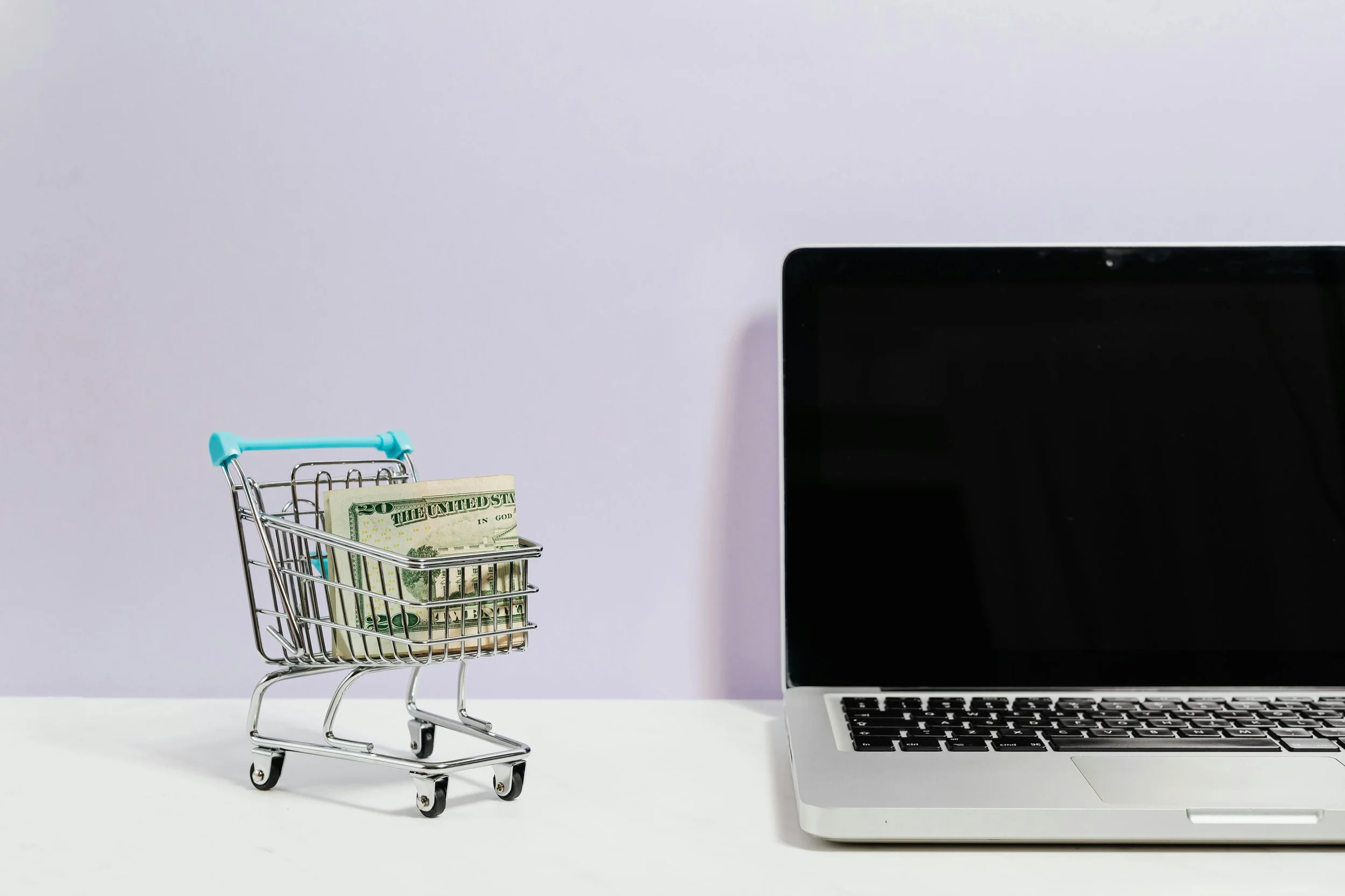 laptop and a mini shopping cart with money on a table