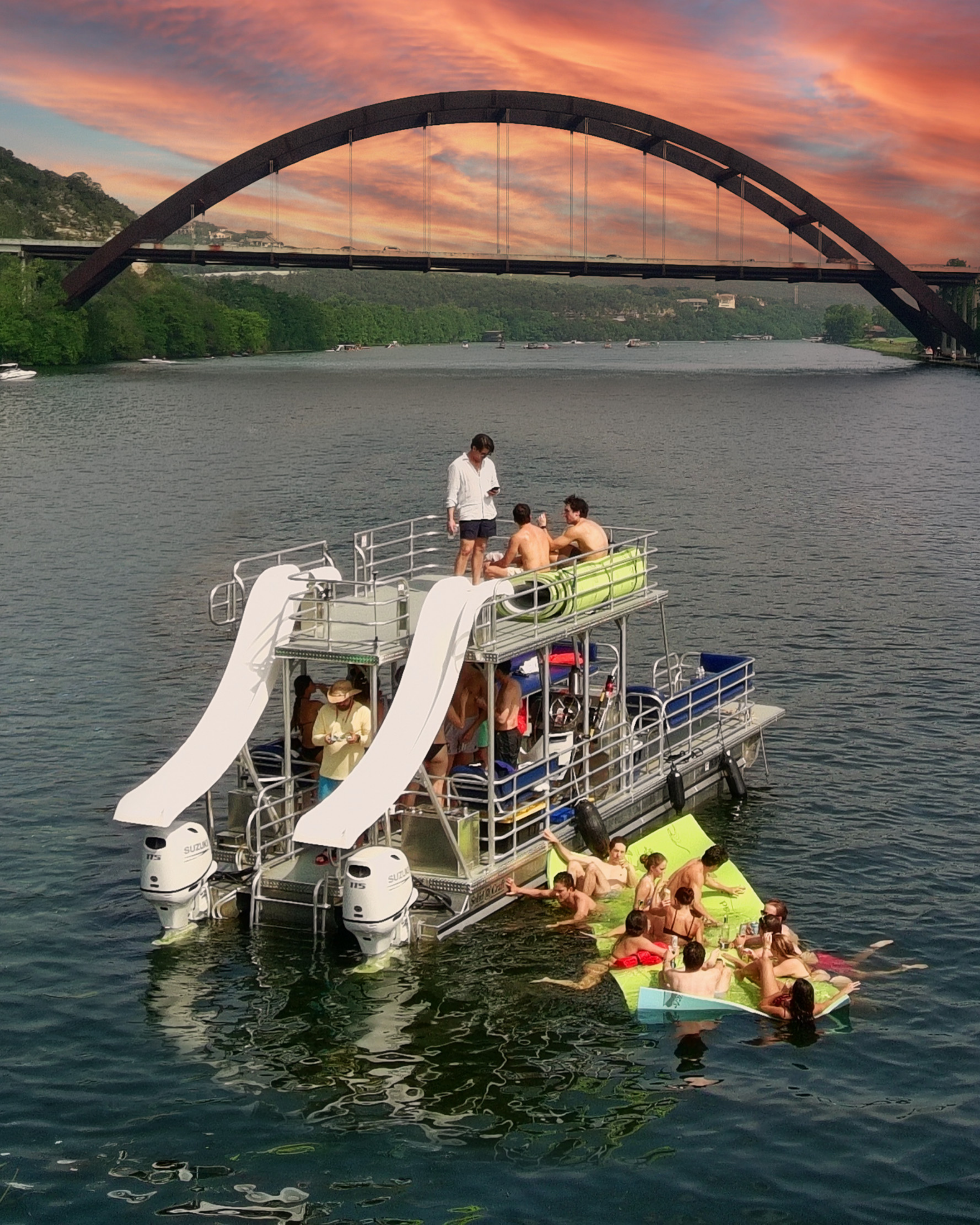 People enjoying themselves on a boat with water slides, surrounded by water, with a bridge in the background and a colorful sky at sunset.