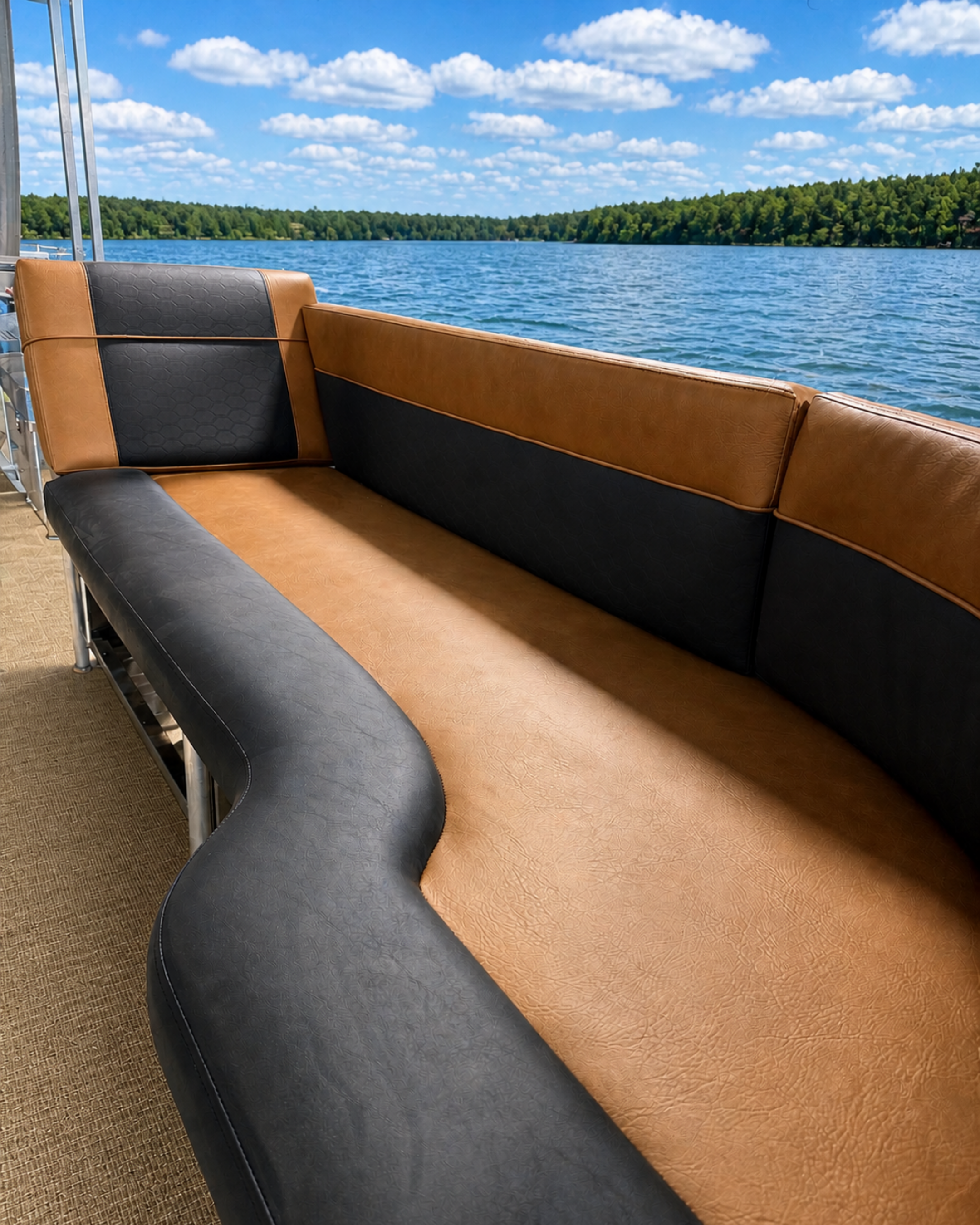 Brown and black cushioned boat seats on a boat overlooking a lake with lush green trees and a blue sky with scattered fluffy clouds.