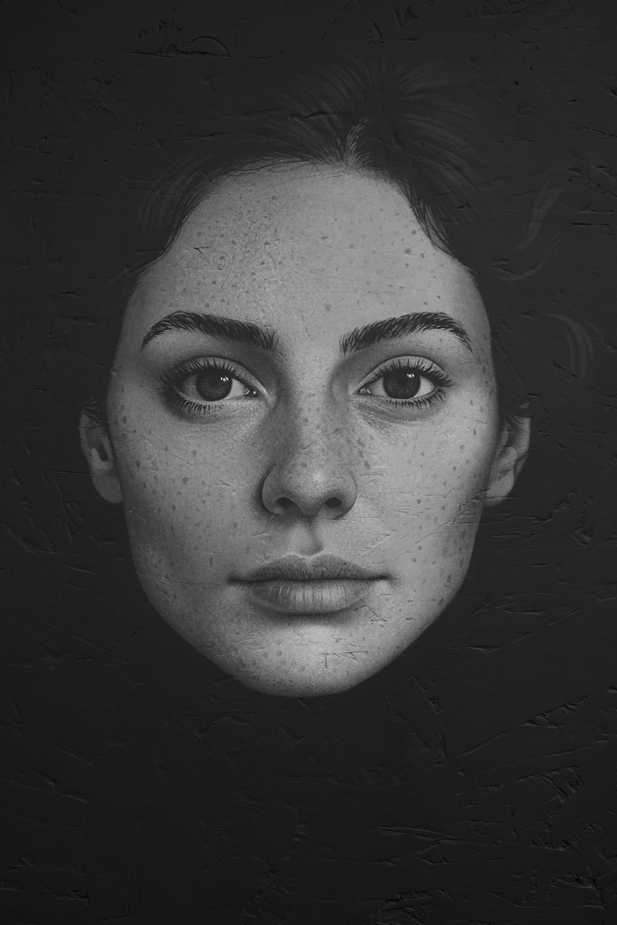 Black and white portrait of a young woman's face with striking features, lips, and freckles, against a dark background.