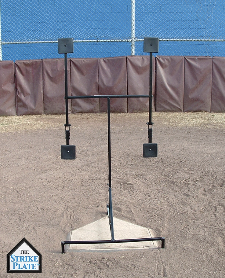 A plastic home plate surrounded by a standing protective barrier, with two small speakers mounted on tall poles on either side, on a baseball field.