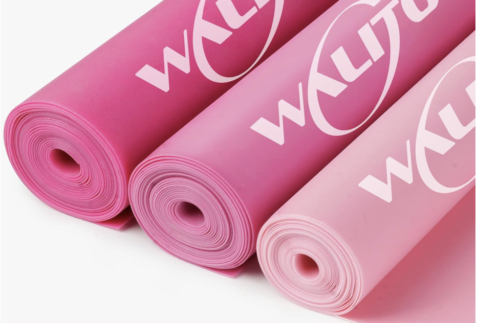 Three pink rolled WACOM yoga mats laying side by side on a white surface