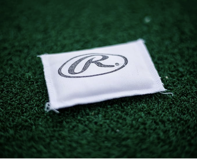 A white cloth with the Rawlings logo lies on green artificial turf.