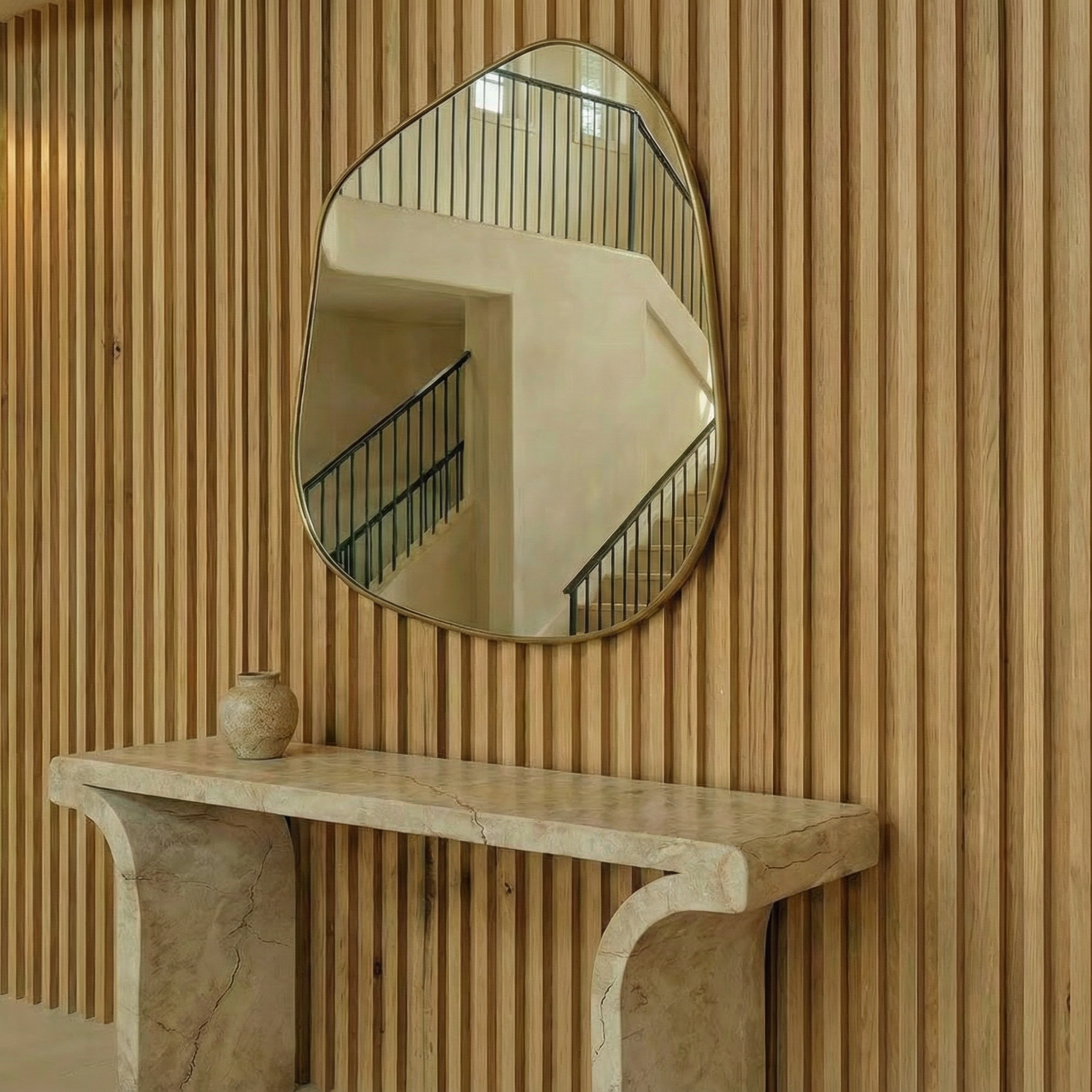 A decorative mirror above a marble console table with a small vase on it, mounted on a wooden slat wall.