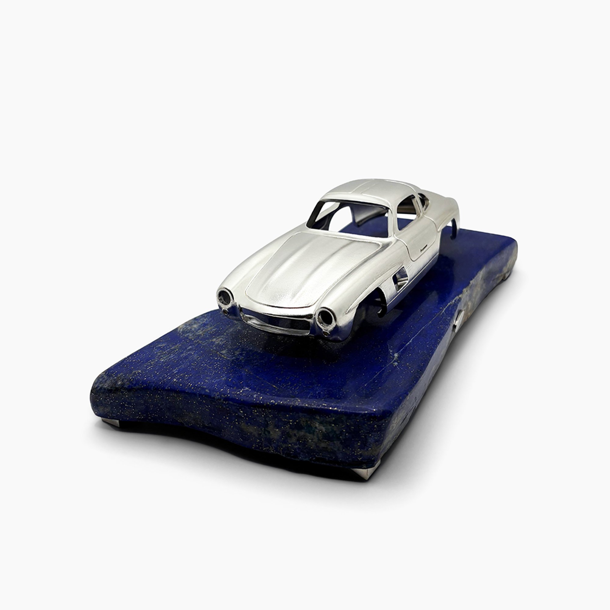 Silver vintage car model placed on a blue stone with a white background.