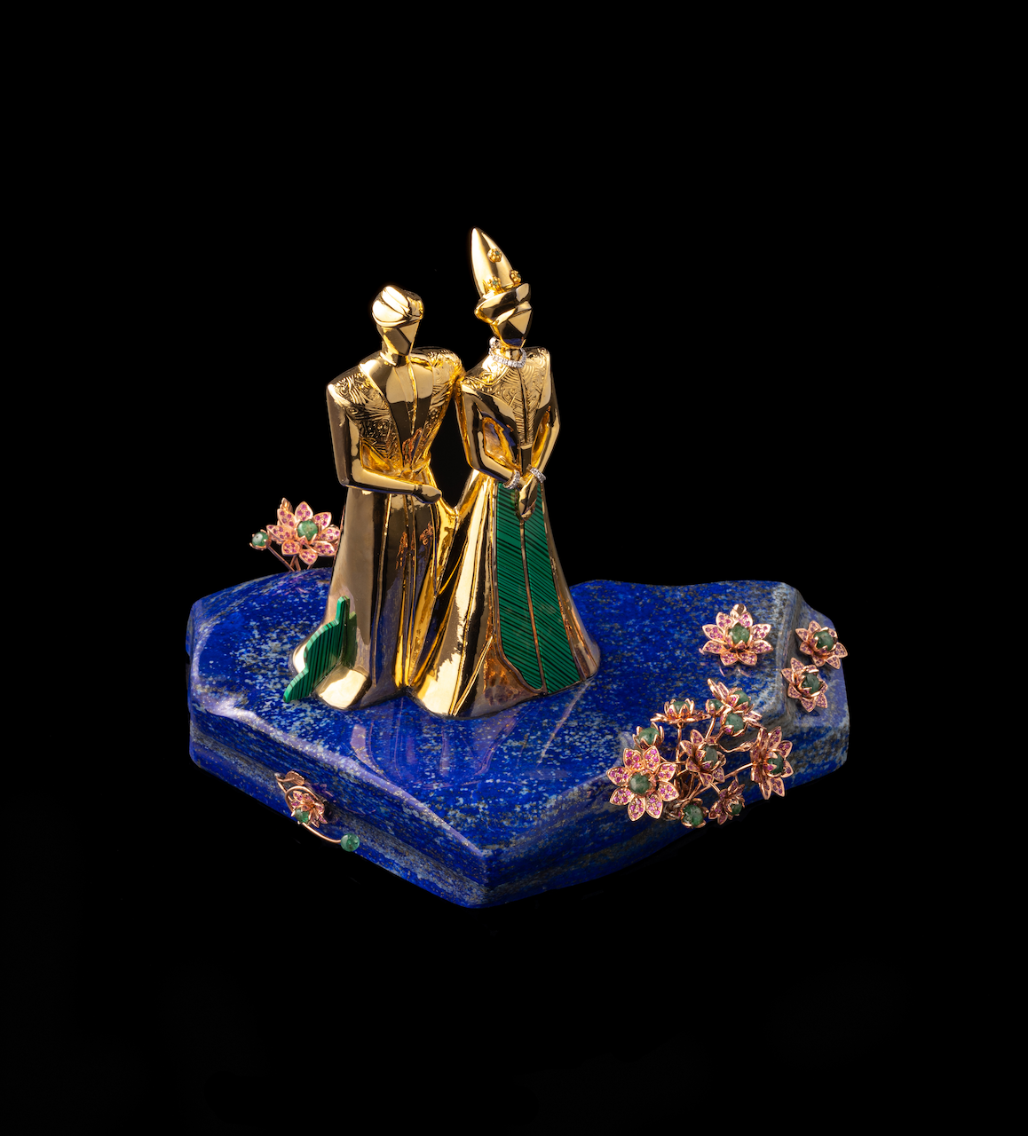 Golden figurines of two people, one wearing a tall hat, standing on a blue stone base decorated with pink and green flower accents