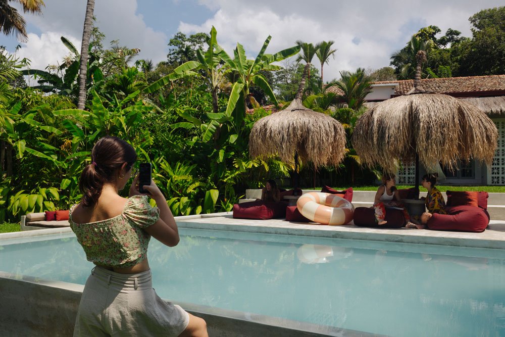 Woman taking a photo of people relaxing by a pool with thatched umbrellas in a tropical setting with lush green foliage — Casa Tikiri, Ahangama, Sri Lanka