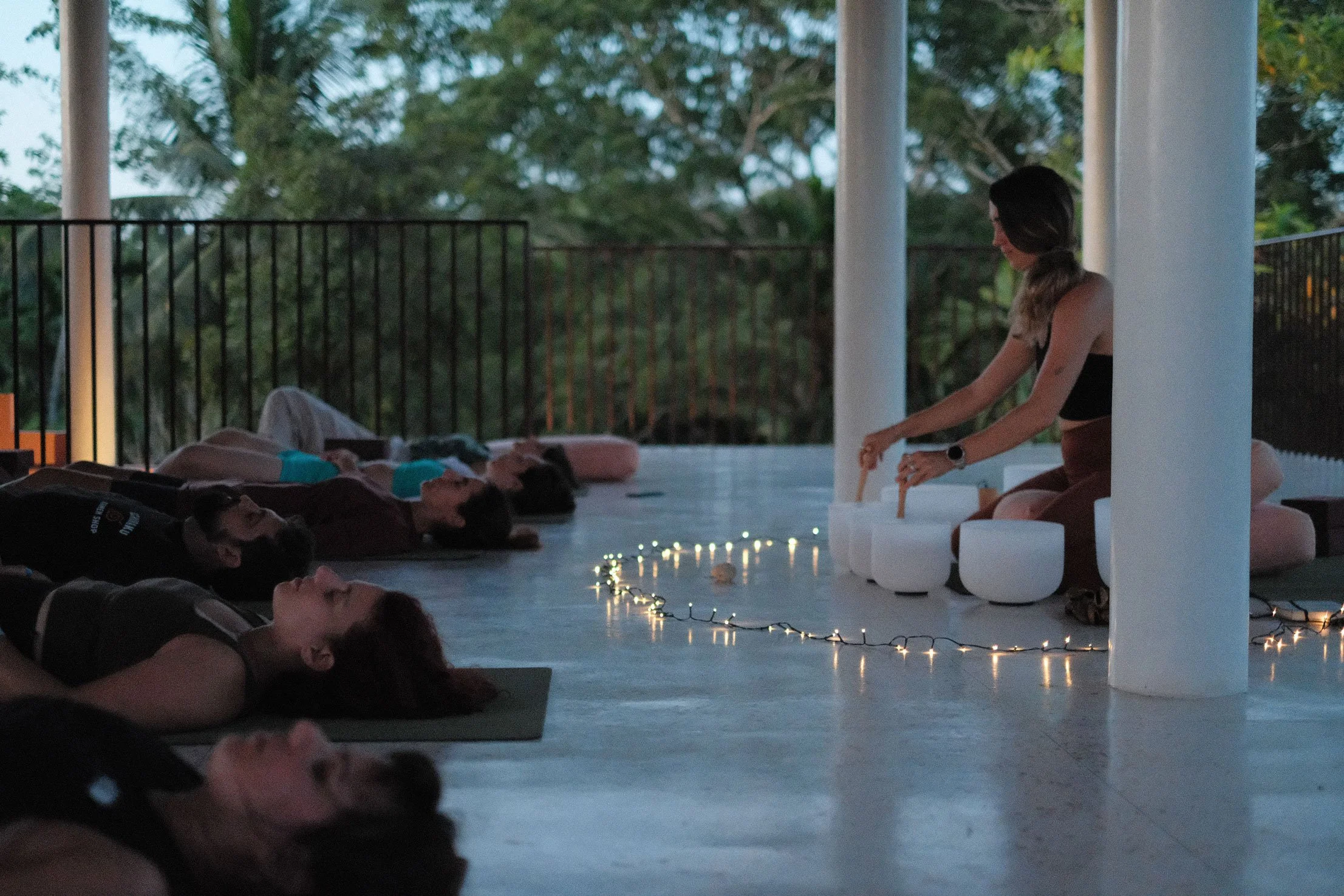 A woman leading a meditation or yoga session outdoors during sunset, with people lying on mats and lights on the ground — Casa Tikiri, Ahangama, Sri Lanka