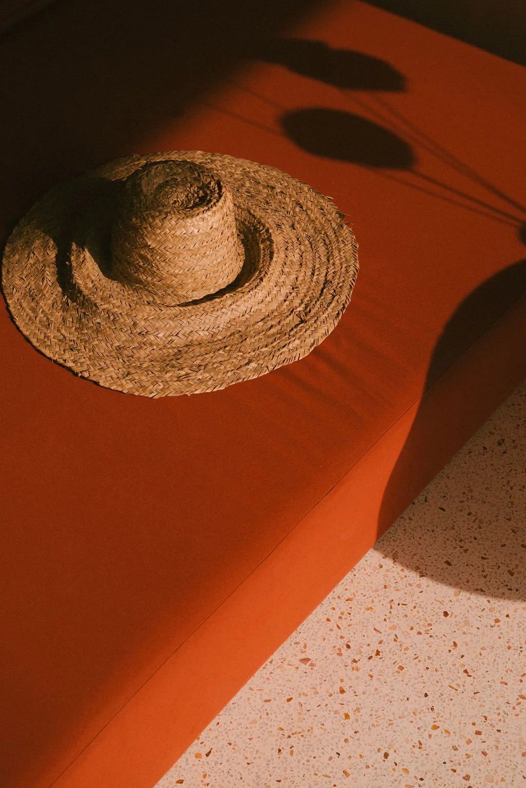 A woven straw sun hat placed on a wooden surface with a shadow cast by a lamp over it. — Casa Tikiri, Ahangama, Sri Lanka