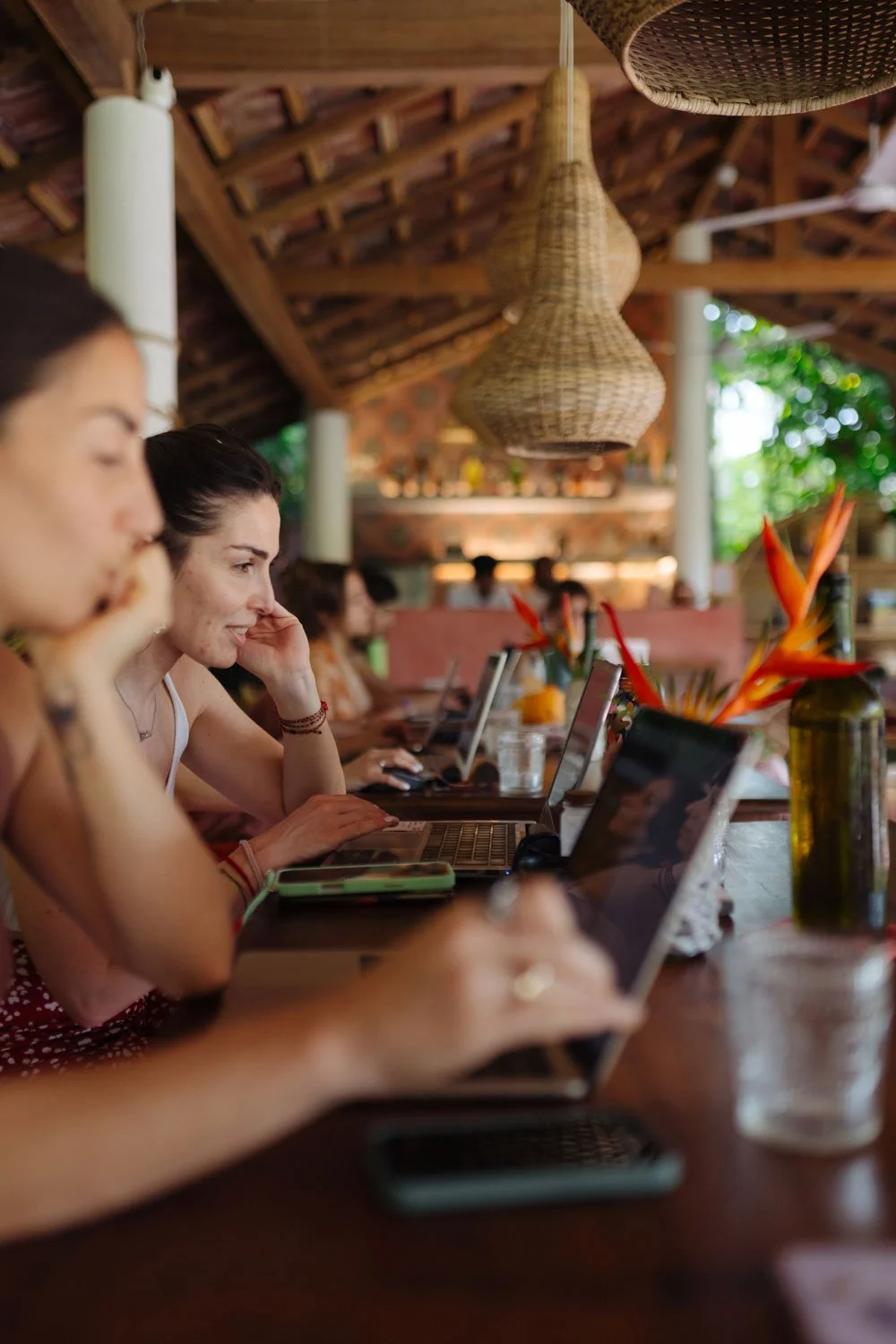 People working on laptops at a long wooden table in a rustic, tropical-themed cafe with hanging wicker lights and lush greenery outside — Casa Tikiri, Ahangama, Sri Lanka
