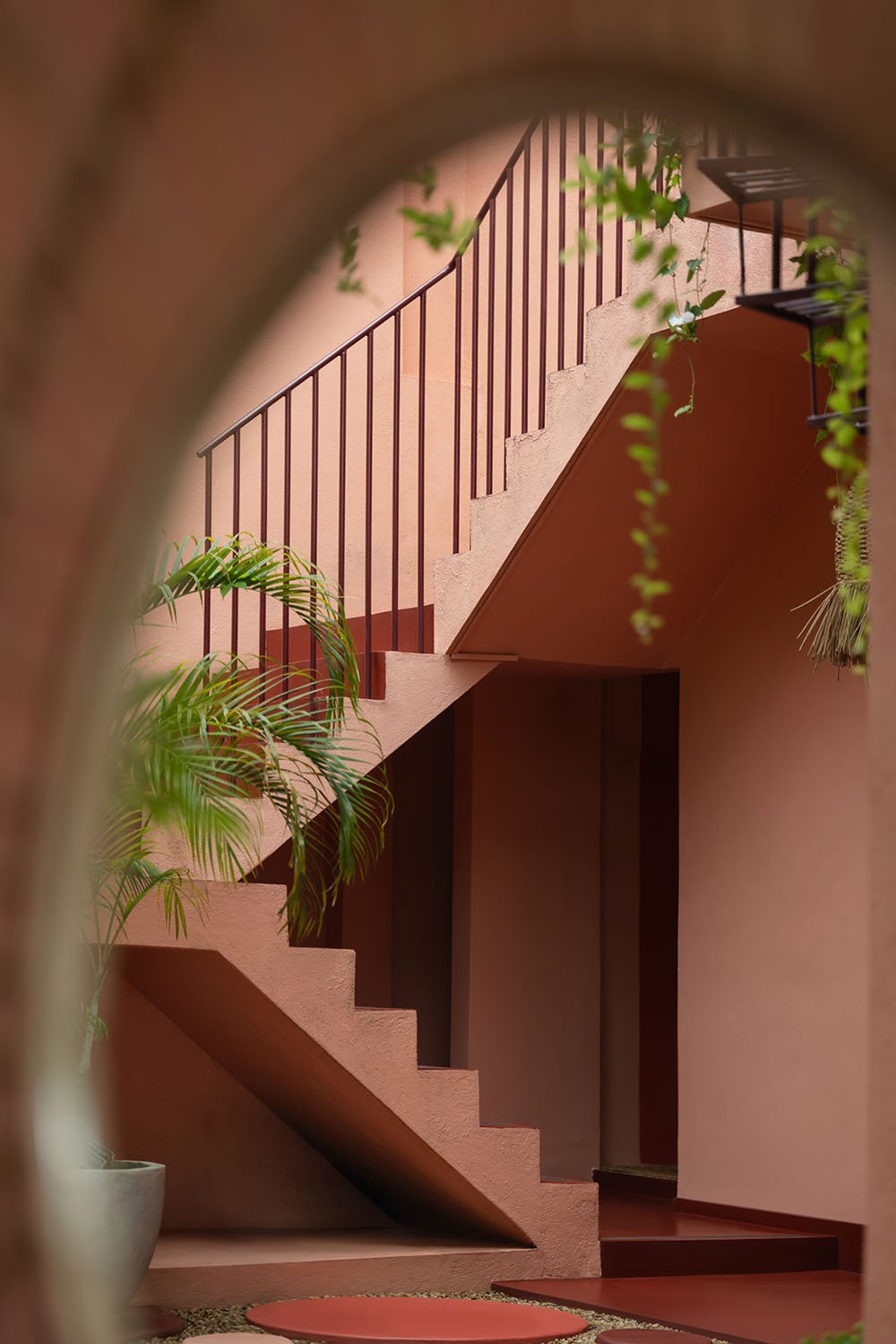 Interior courtyard with pink stairway and black railing, framed by an arch, with green potted plants and hanging greenery — Casa Tikiri Paddy Lodge, Ahangama, Sri Lanka