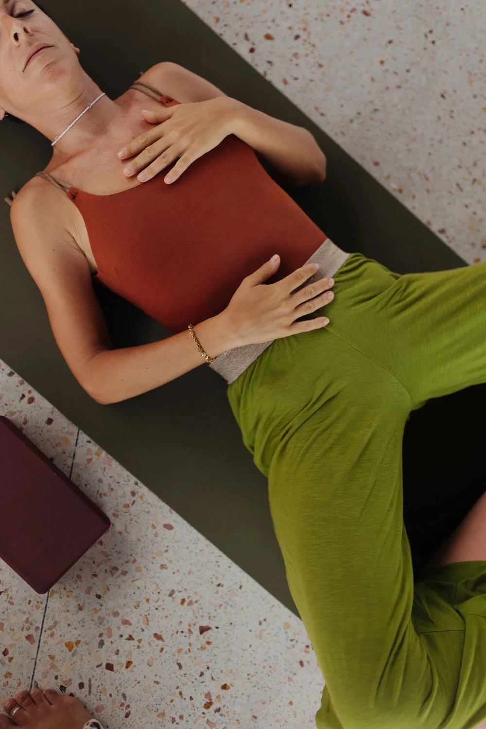 Woman lying on her back, holding her chest with one hand and her stomach with the other, on a yoga mat in a fitness or studio setting — Casa Tikiri, Ahangama, Sri Lanka