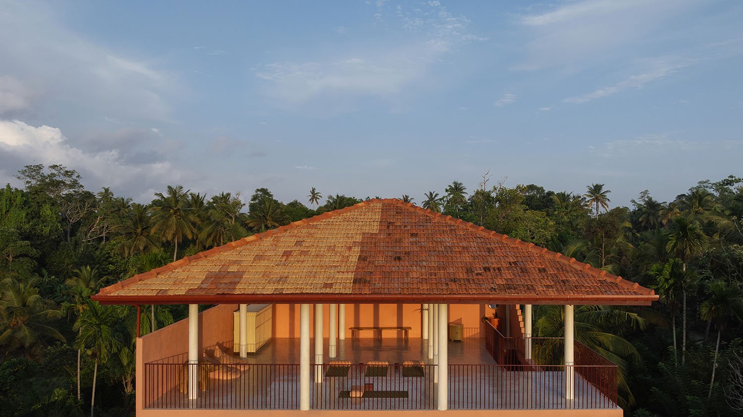 View of a rooftop terrace with red and orange clay tiles, surrounded by a metal railing, overlooking a tropical forest with palm trees under a blue sky with some clouds - Casa Tikiri Paddy Lodge, Ahangama, Sri Lanka