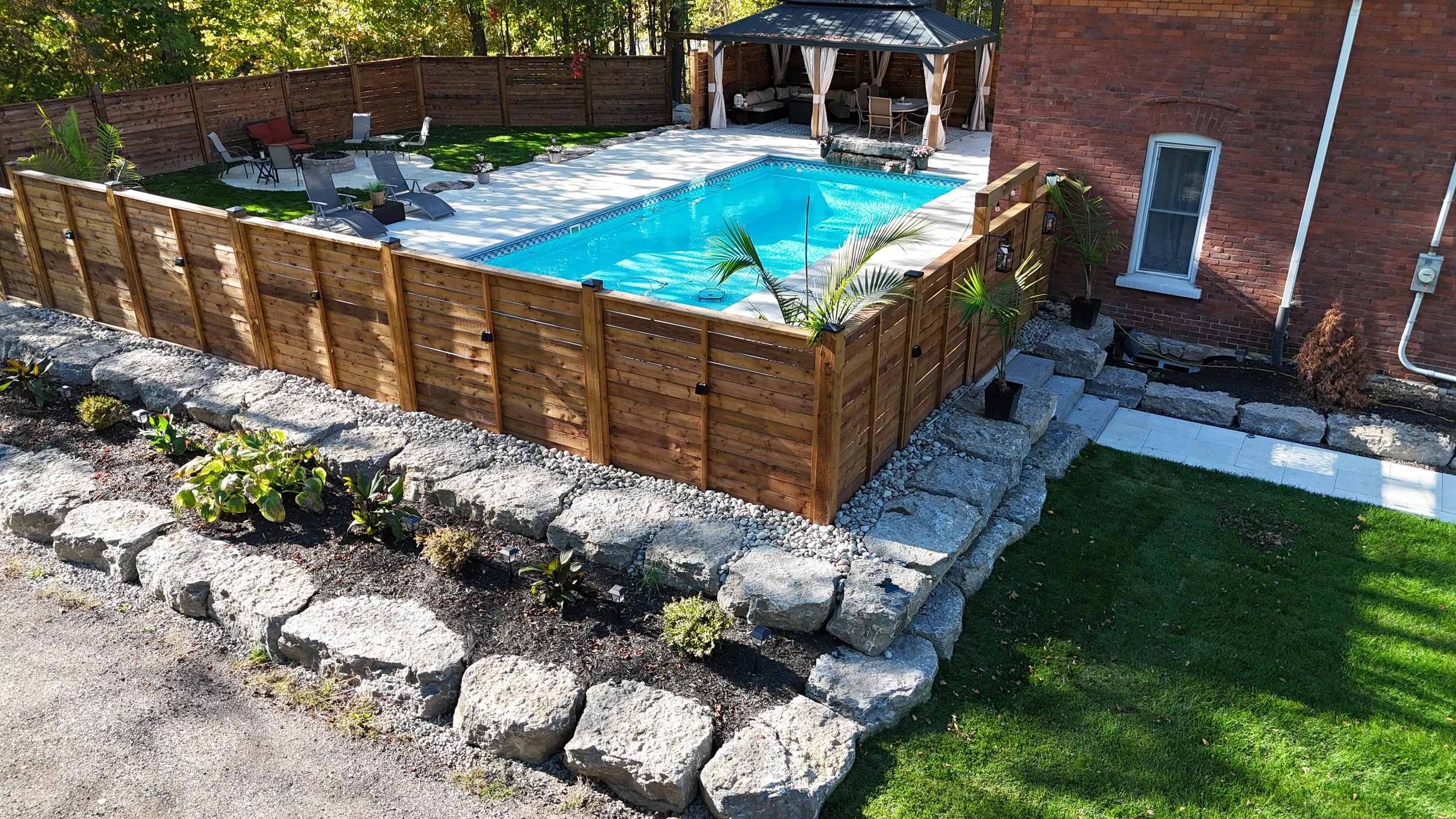 FoxCon hardscape project featuring a pool patio, armour stone retaining walls, steps and finished landscaping near Midland, Ontario.