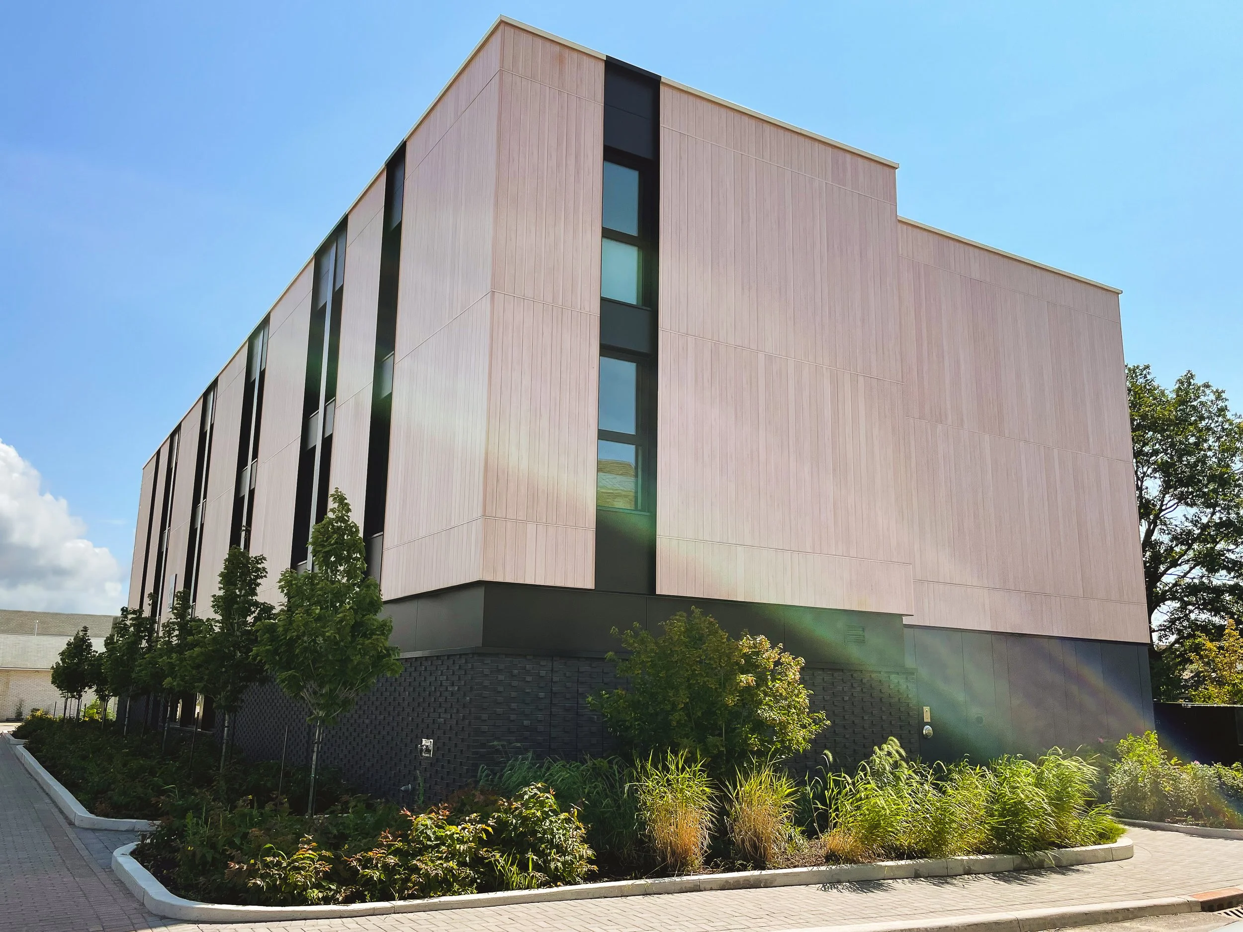 Digital Architectural mockup of modern rectangular building with custom wood paneling on the sides divided by vertically stacked windows along the side and vertical wood paneling enclosed entrance.