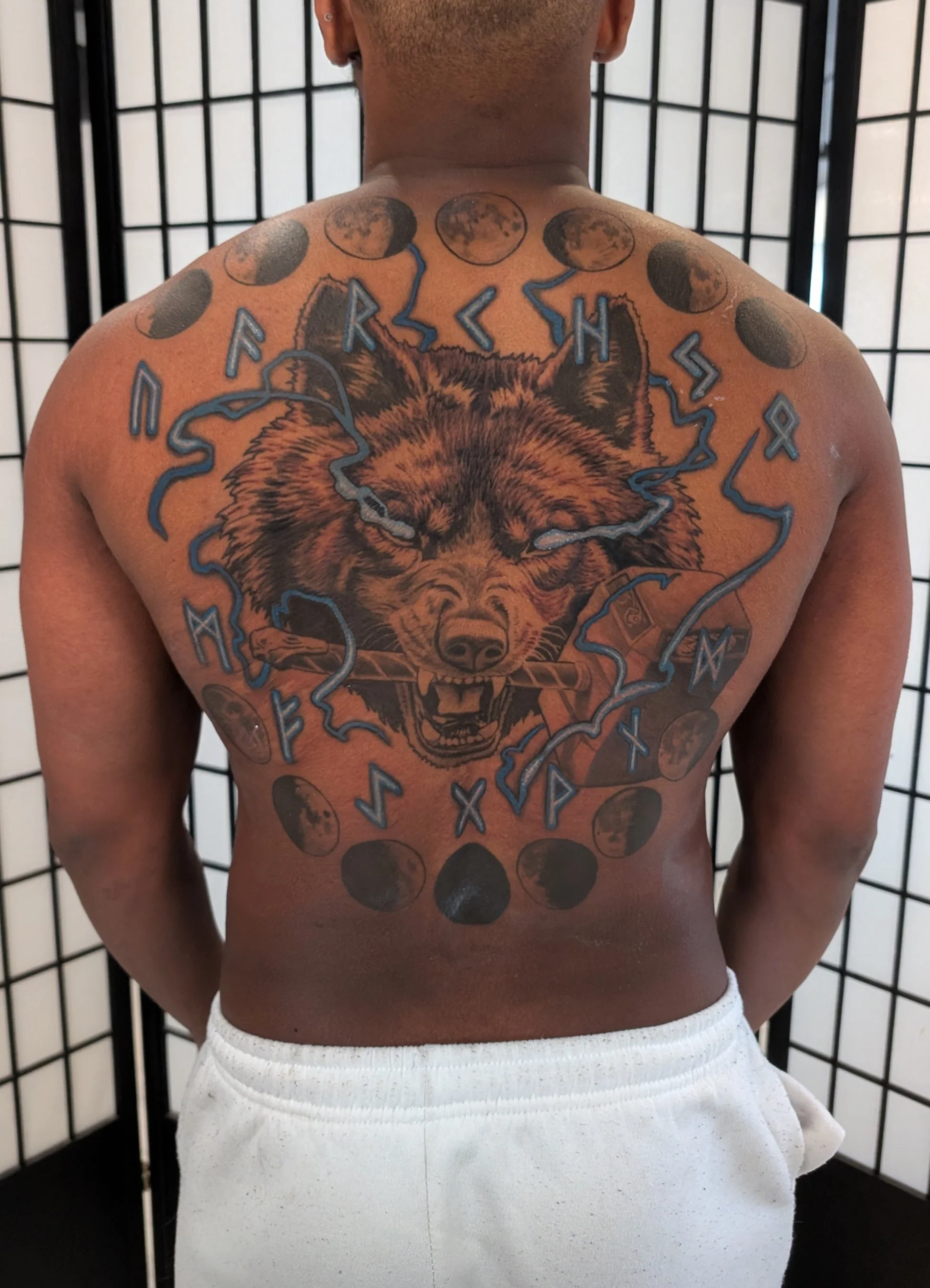 Full back tattoo of wolf runes and blue lighting