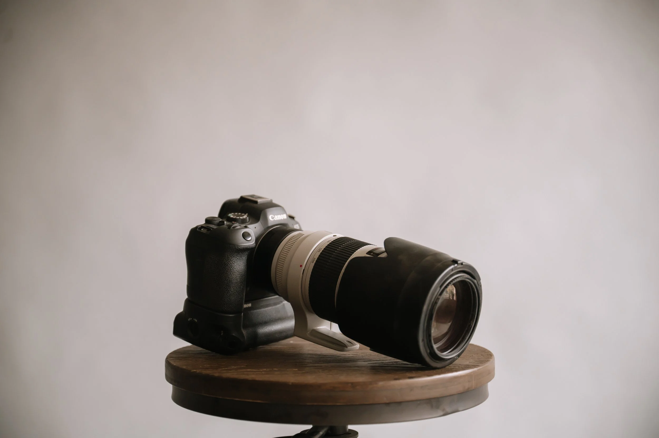 A professional DSLR camera with a large zoom lens mounted on a wooden stool against a plain background.