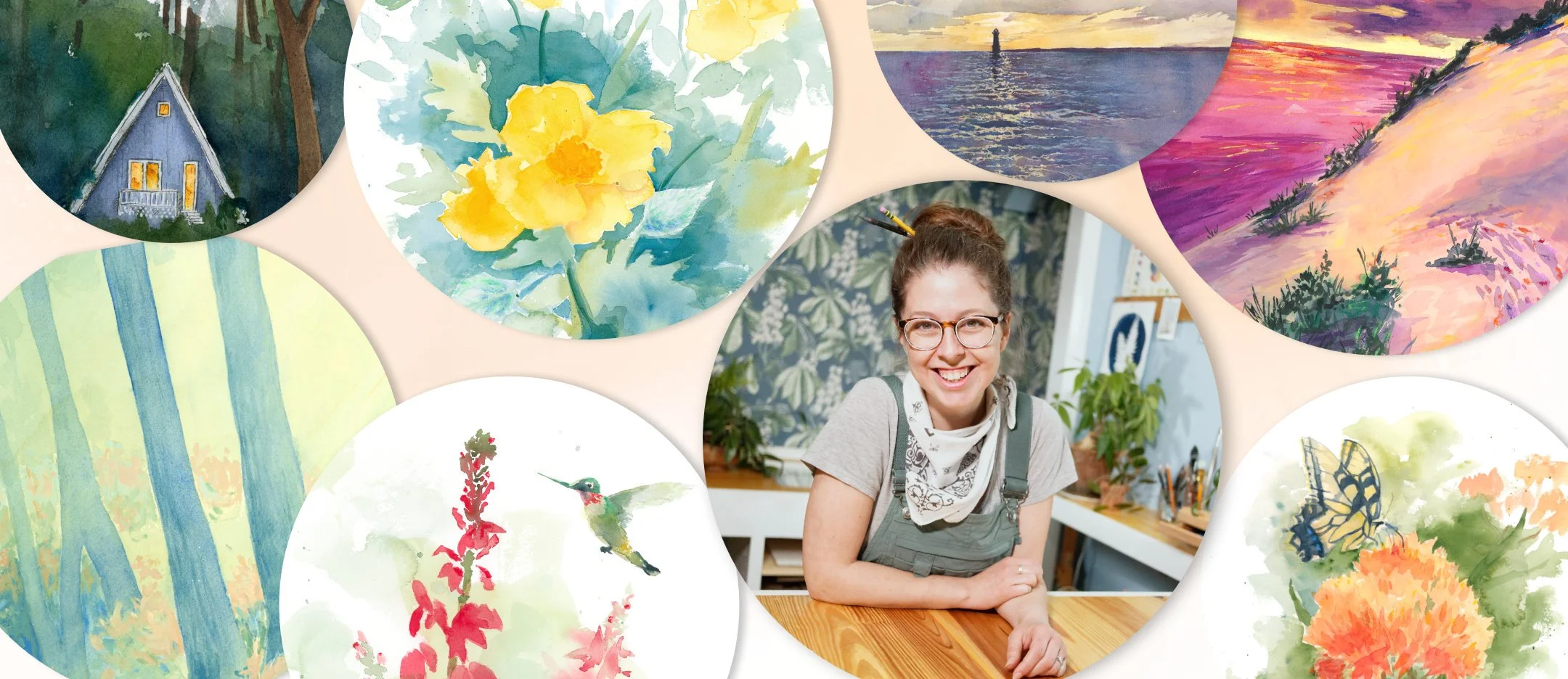 Artist Elizabeth Manning, a smiling woman with glasses and a bandana around her neck sitting at a wooden table in an art studio, surrounded by various watercolor paintings of nature scenes, plants, animals, and landscapes.