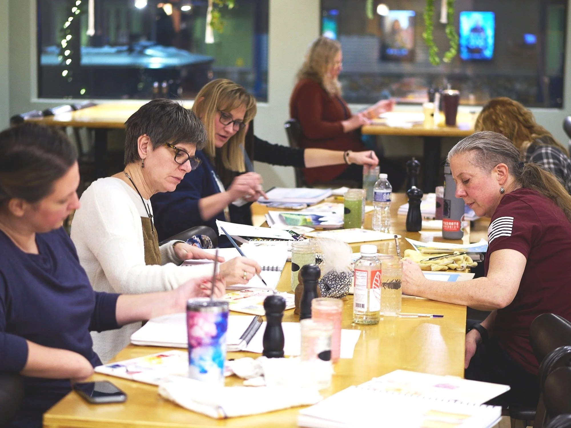 A group of women taking a watercolor class through Two Hoots Studio sitting at a long table.