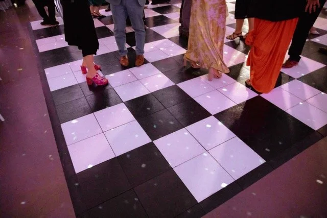 People standing on a black and white checkered dance floor with some wearing traditional clothing and holding shoes.