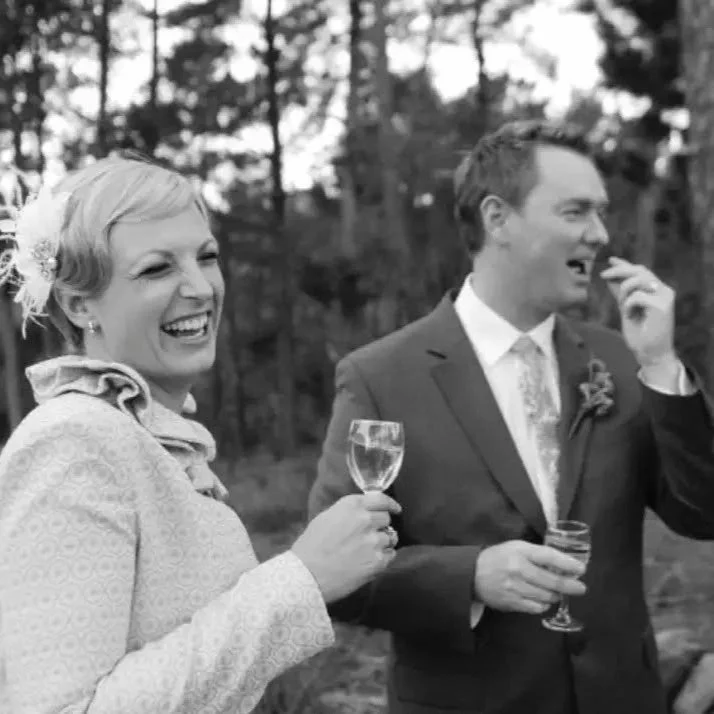 Smiling woman in wedding dress holding a champagne glass, man in suit drinking from a glass at outdoor outdoor wedding celebration