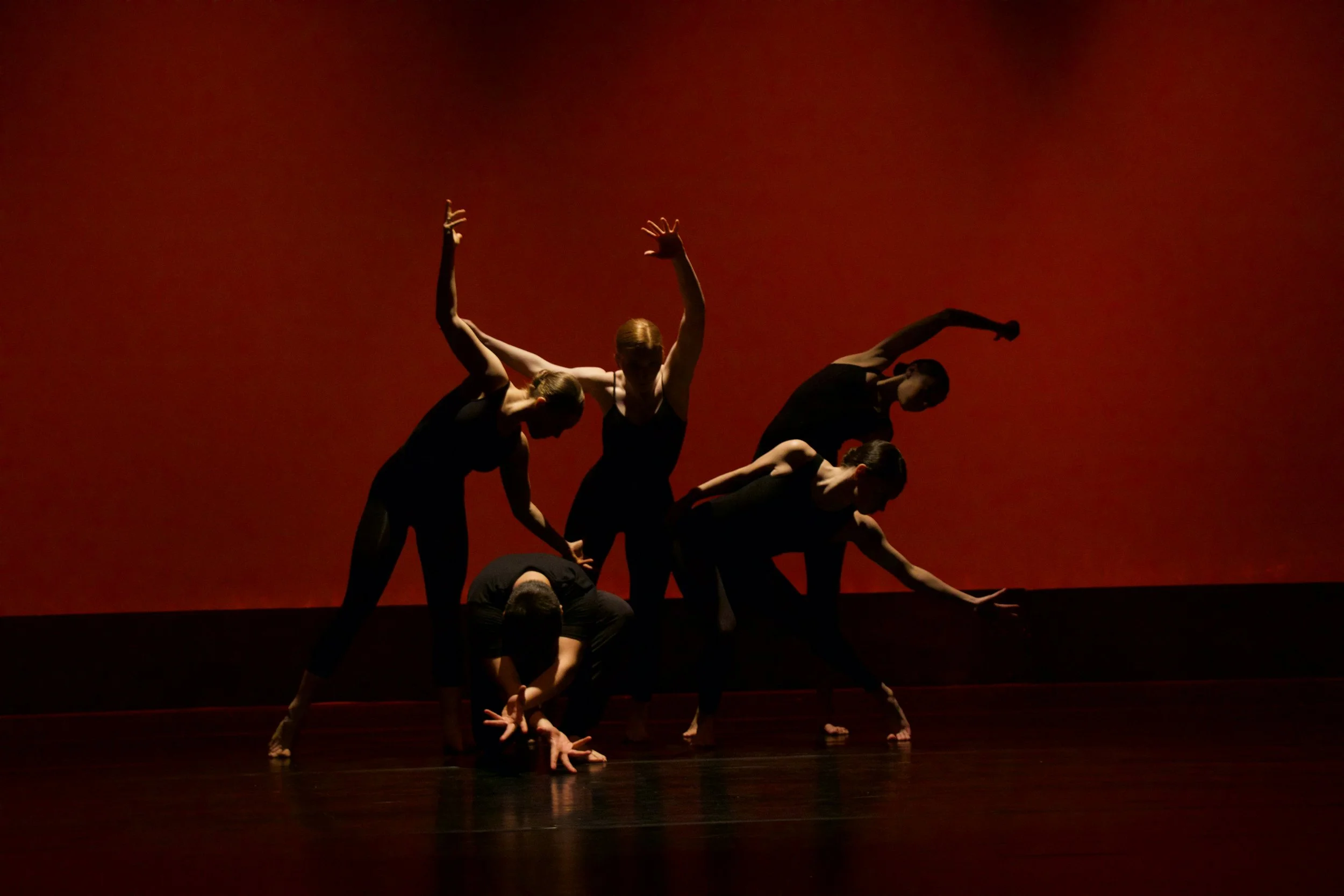Five dancers in a dramatic pose in front of a red background