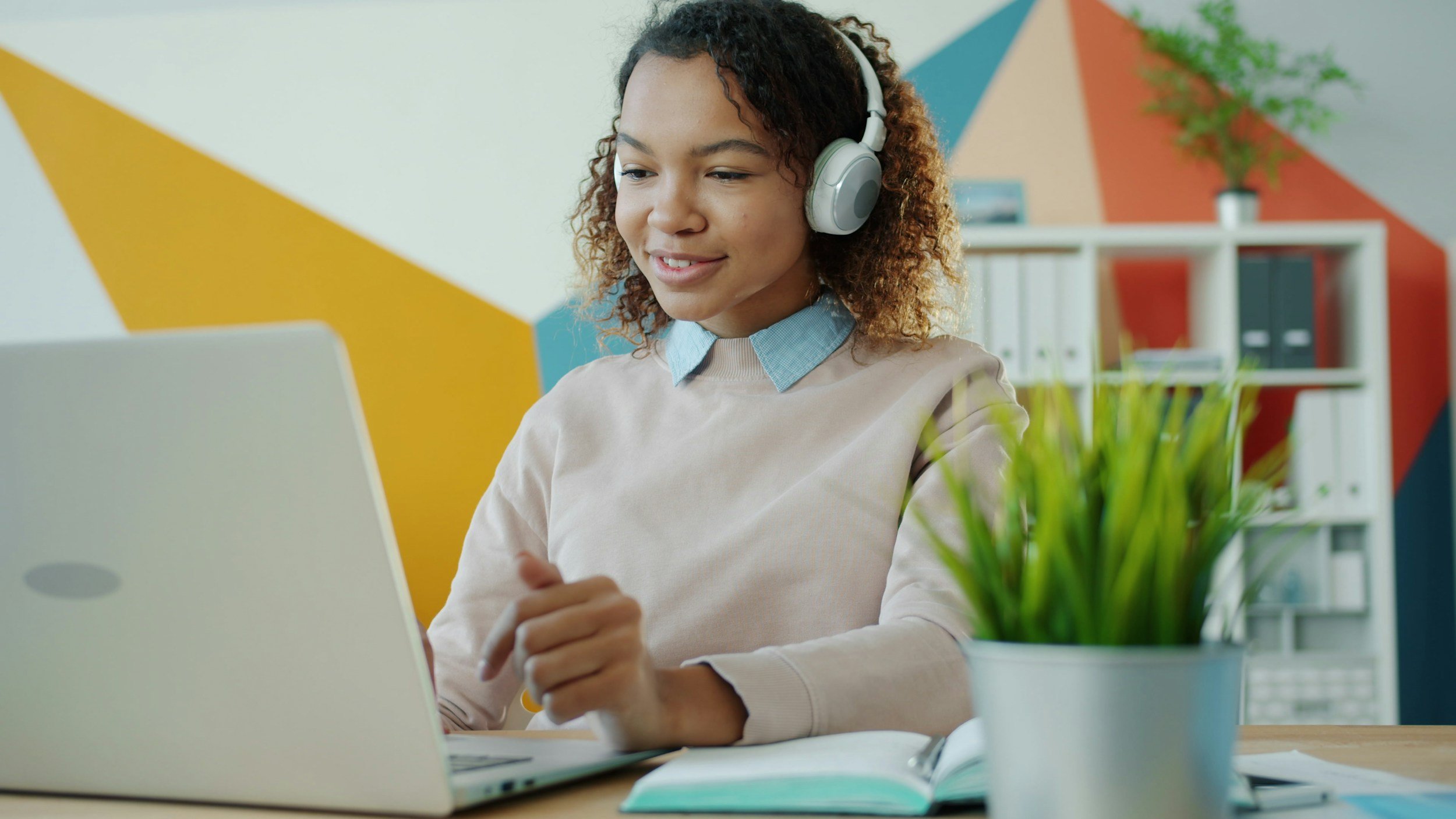 girl sitting at desk with her headphones on looking at a laptop