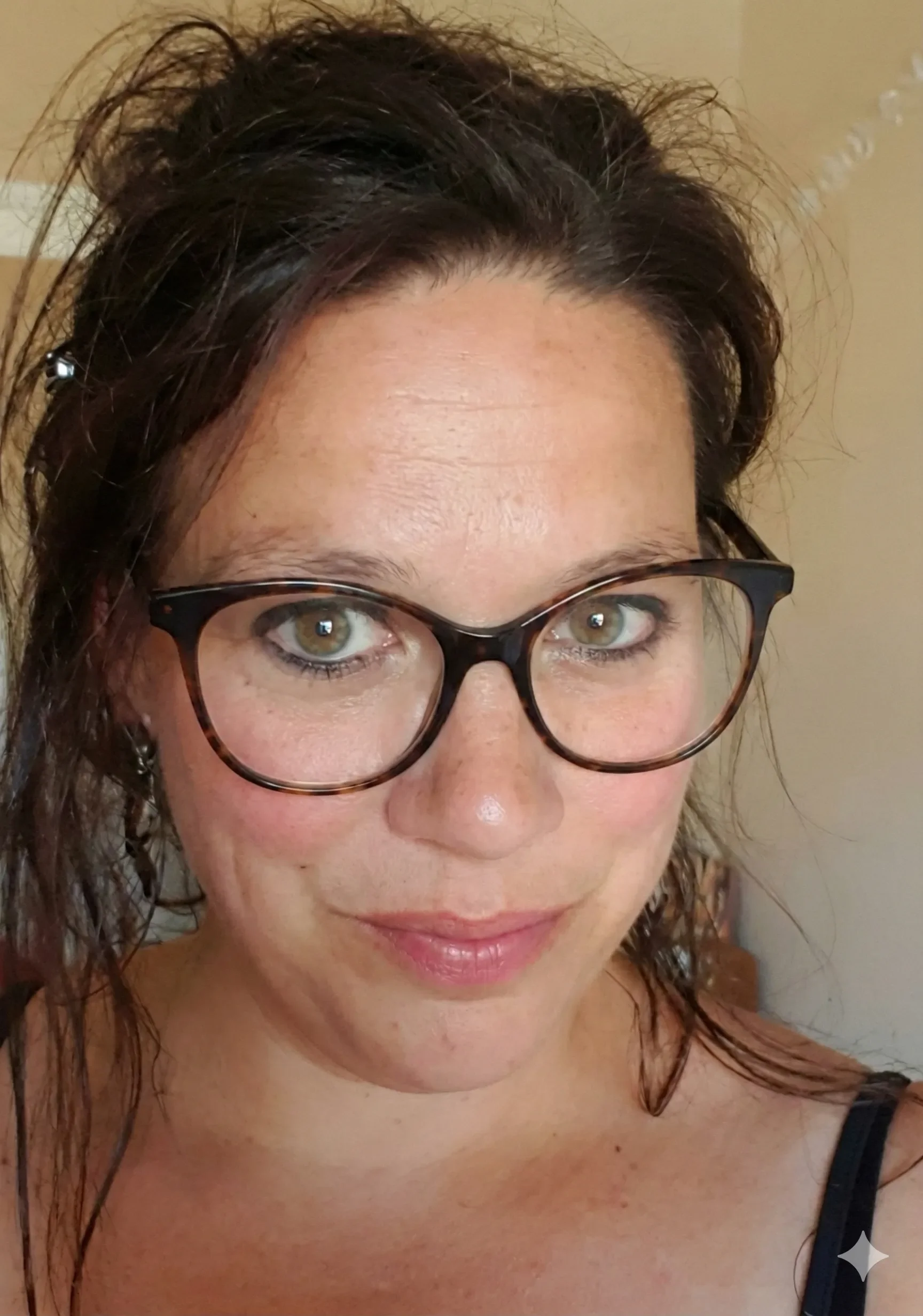 Sylvie, een verpleegster van care4U uit assent met bruin gekruld haar, groene ogen, getint gezicht, zwarte bril en een zwarte top.