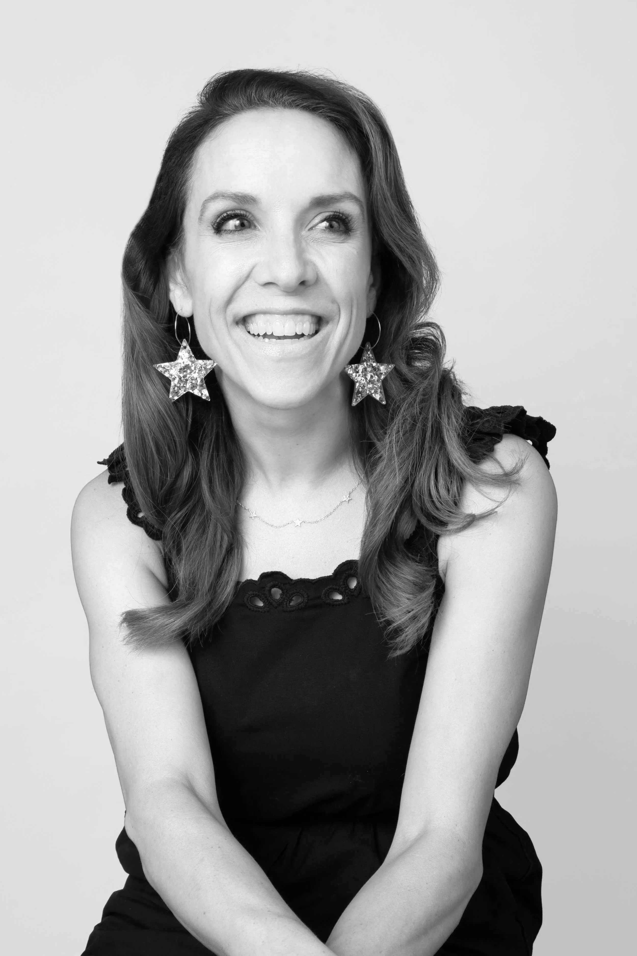 Black and white photo of a woman with long wavy hair, star-shaped earrings, smiling and looking to her left, against a plain background.