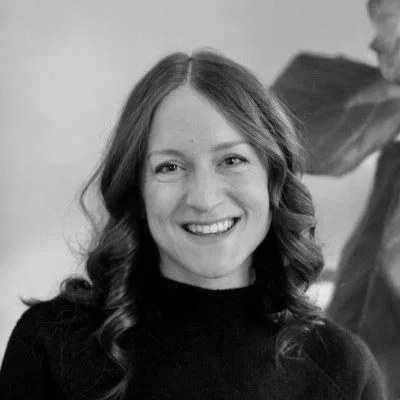 Black and white portrait of a woman with long dark hair, smiling, wearing a textured sweater, against a plain background.