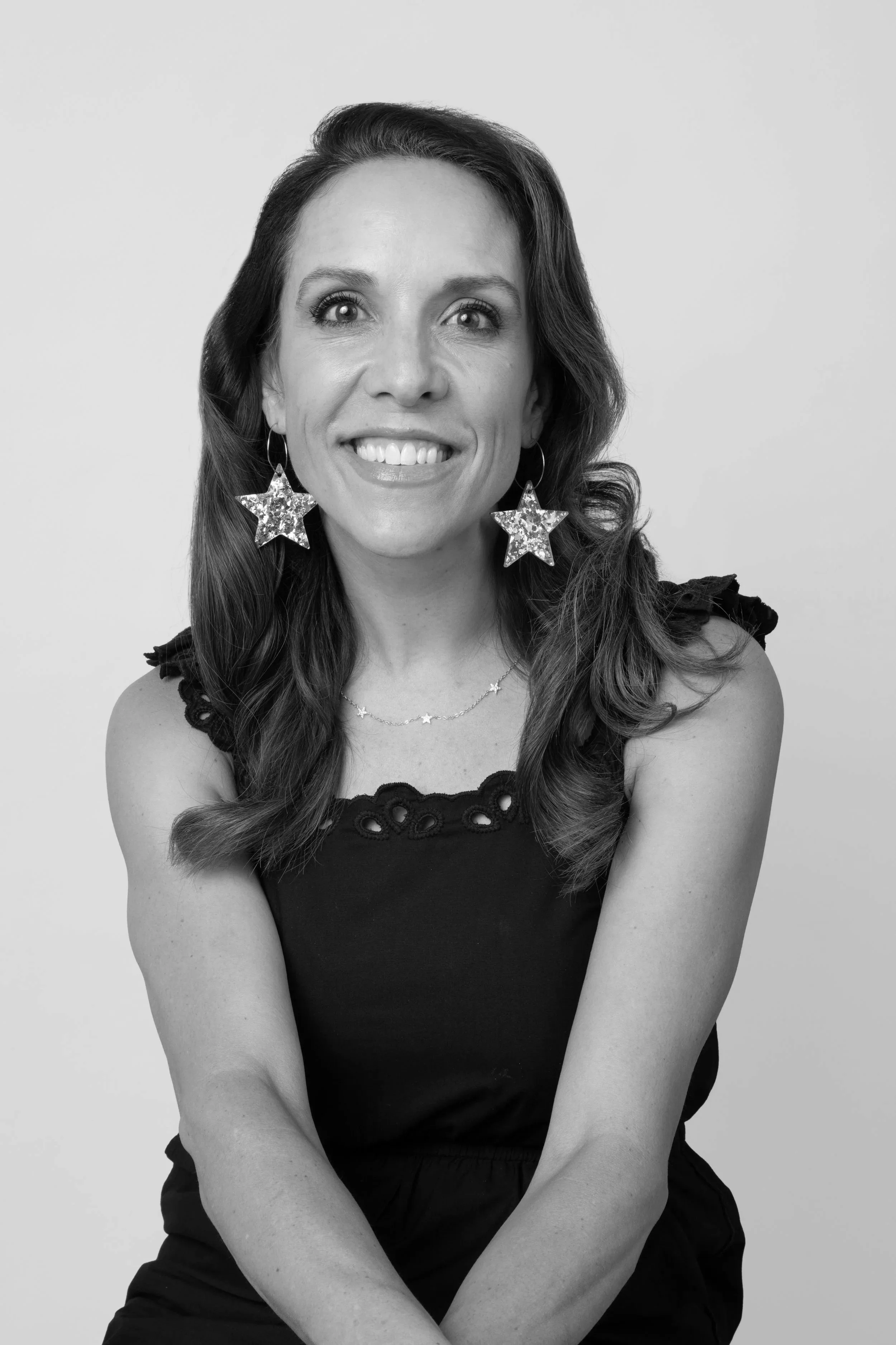 Black and white photo of a woman with long wavy hair, star-shaped earrings, smiling and looking to her left, against a plain background.