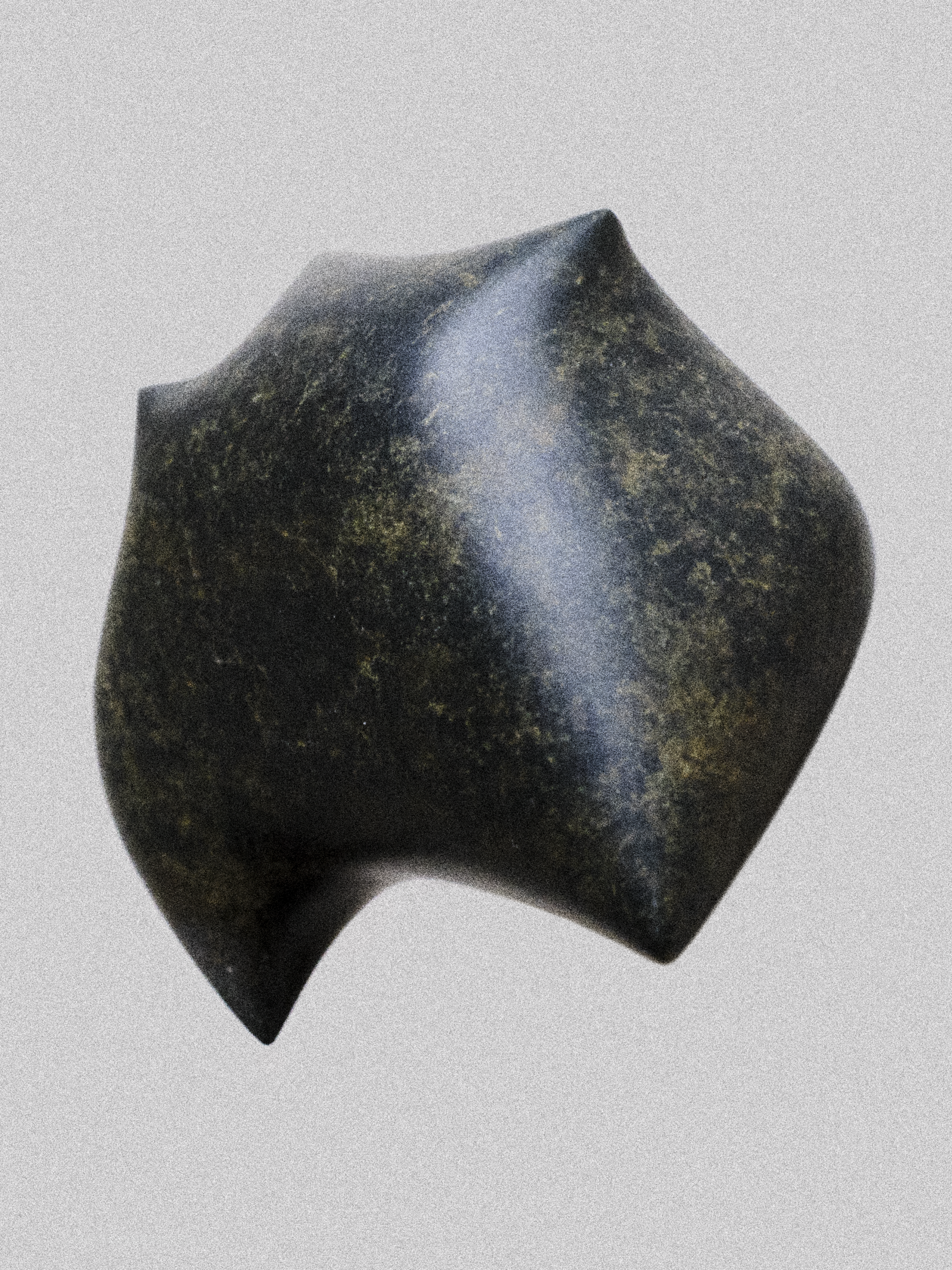 A black, textured, geometric-shaped stone or artifact with a tapers to a pointed end, placed on a plain light gray background.