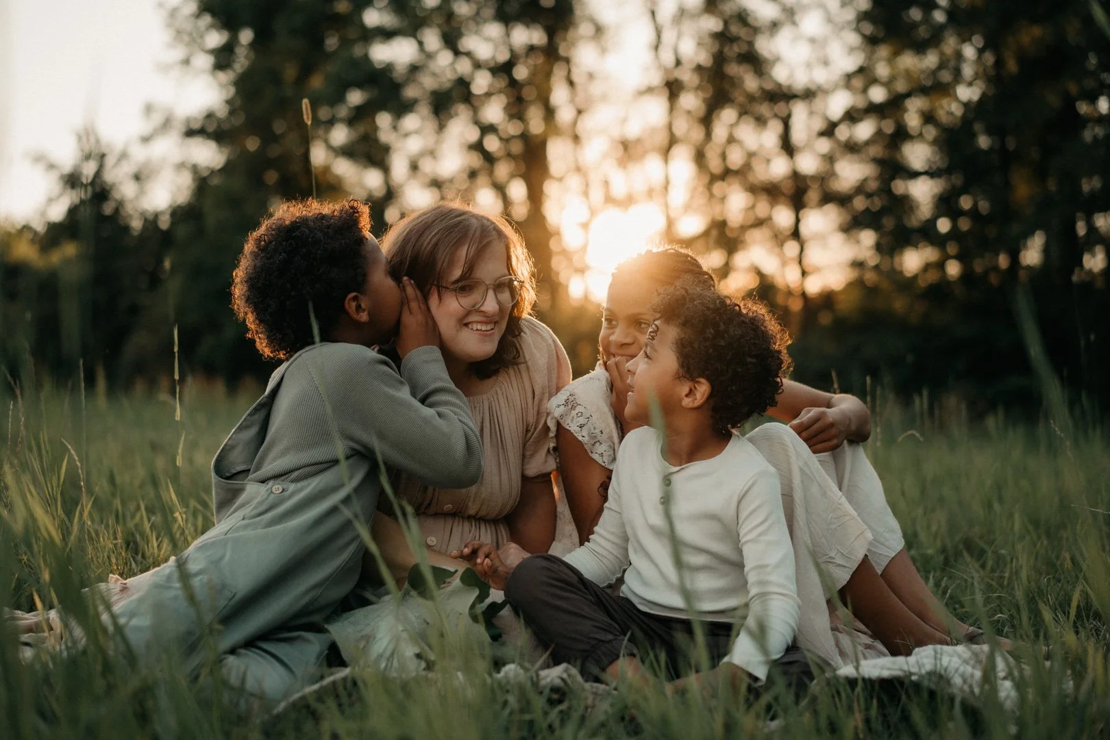 Mama sitzt mit ihren Kindern auf der Wiese im Abendlicht