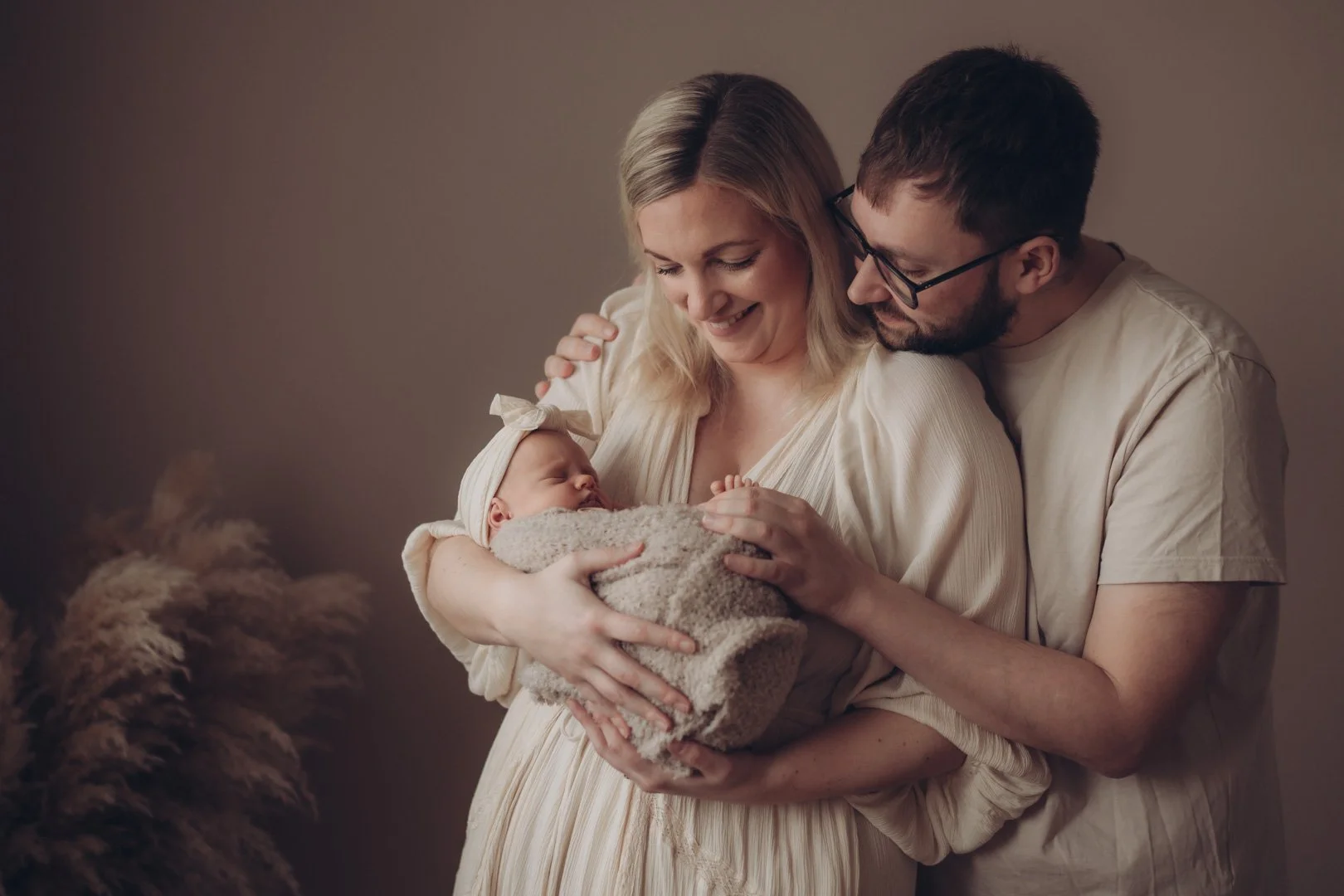Glückliche Eltern halten ihr neugeborenes Baby im Arm und kuscheln miteinander.