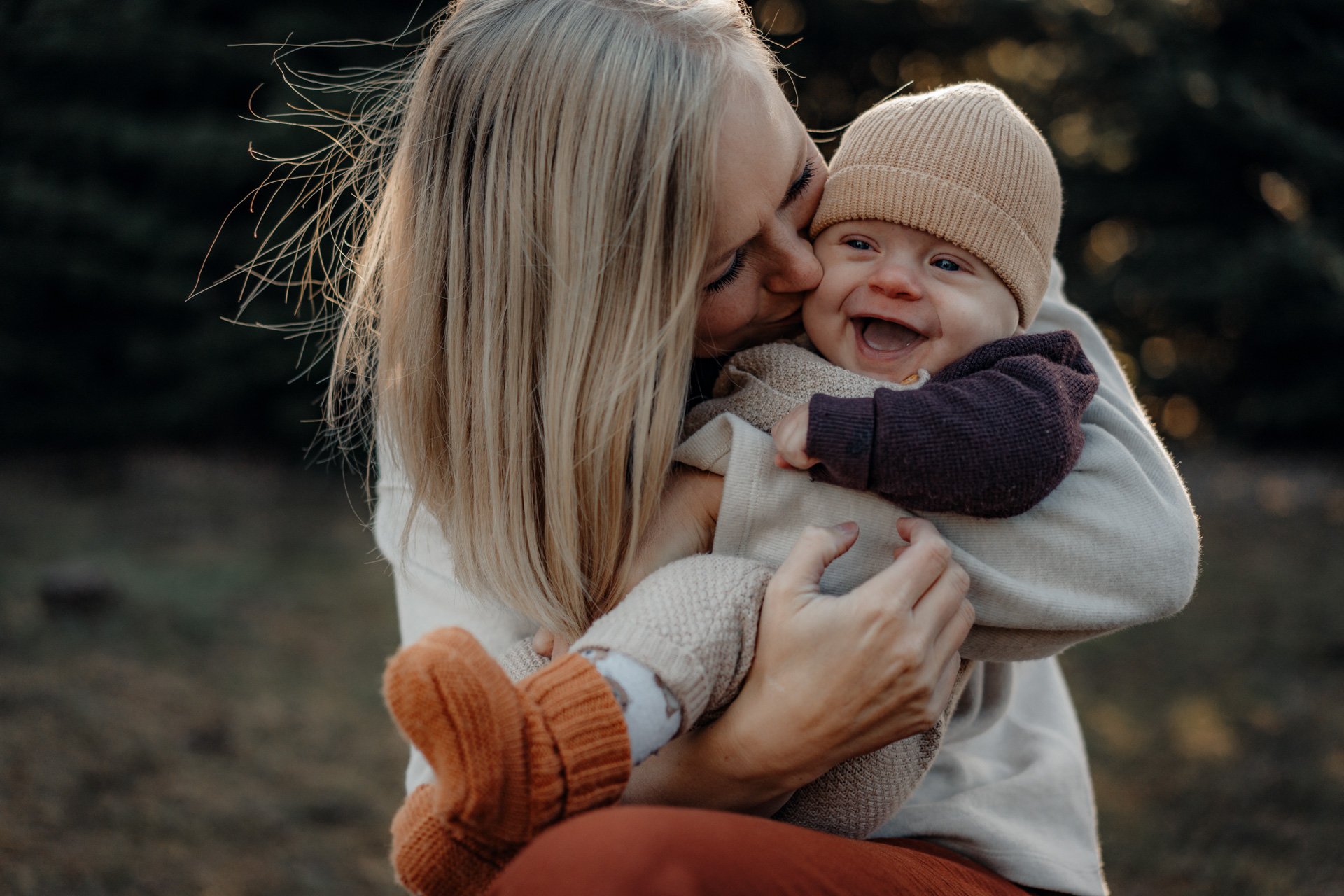 Mama kuschelt mit Baby draußen im warmen Licht.