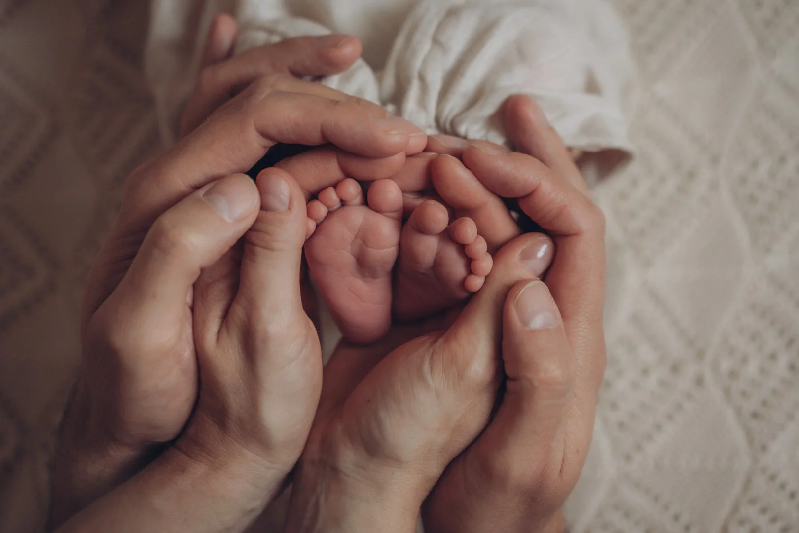 Eltern umschließen liebevoll mit ihren Händen die kleinen Füßchen ihres Babys.