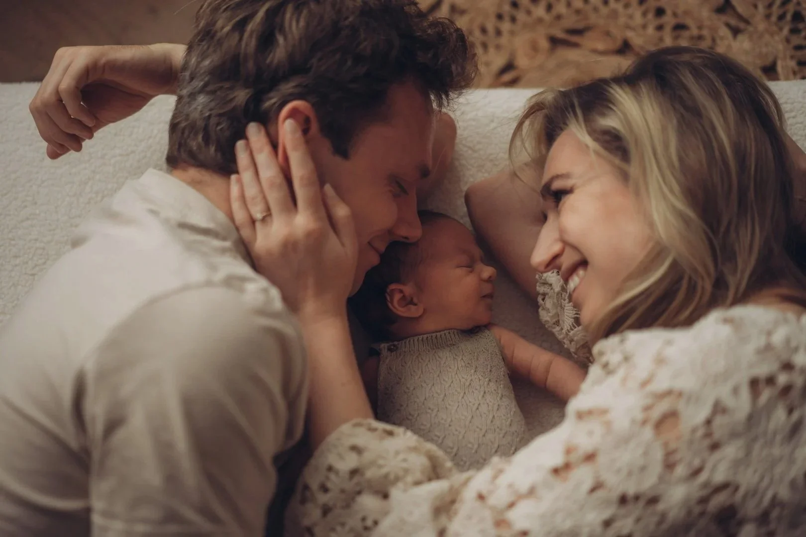 Eltern liegen mit ihrem neugeborenen Baby im Bett und kuscheln zusammen.