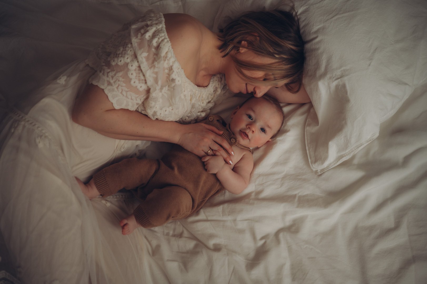 Baby und Mama liegen kuschelnd zusammen im Bett.