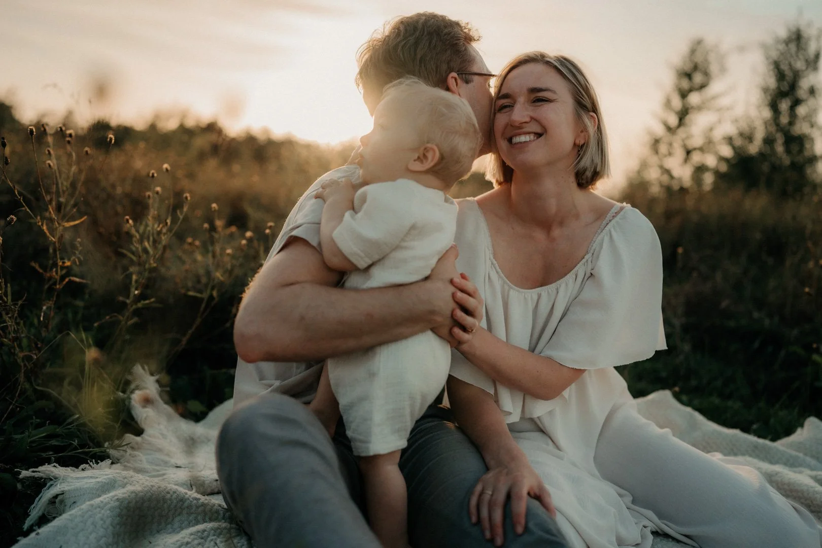 Eltern und Baby kuscheln zusammen auf einer Decke im Sonnenuntergang.