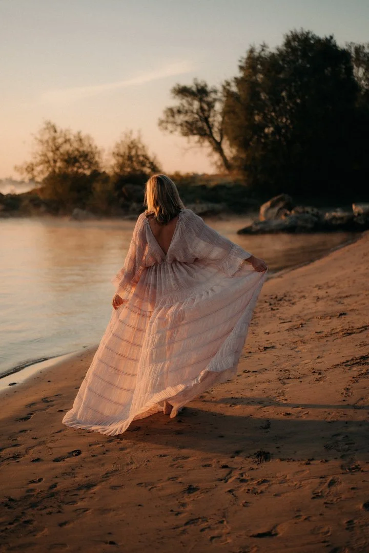Schwangere hält ihr Kleid am Strand im Sonnenaufgang