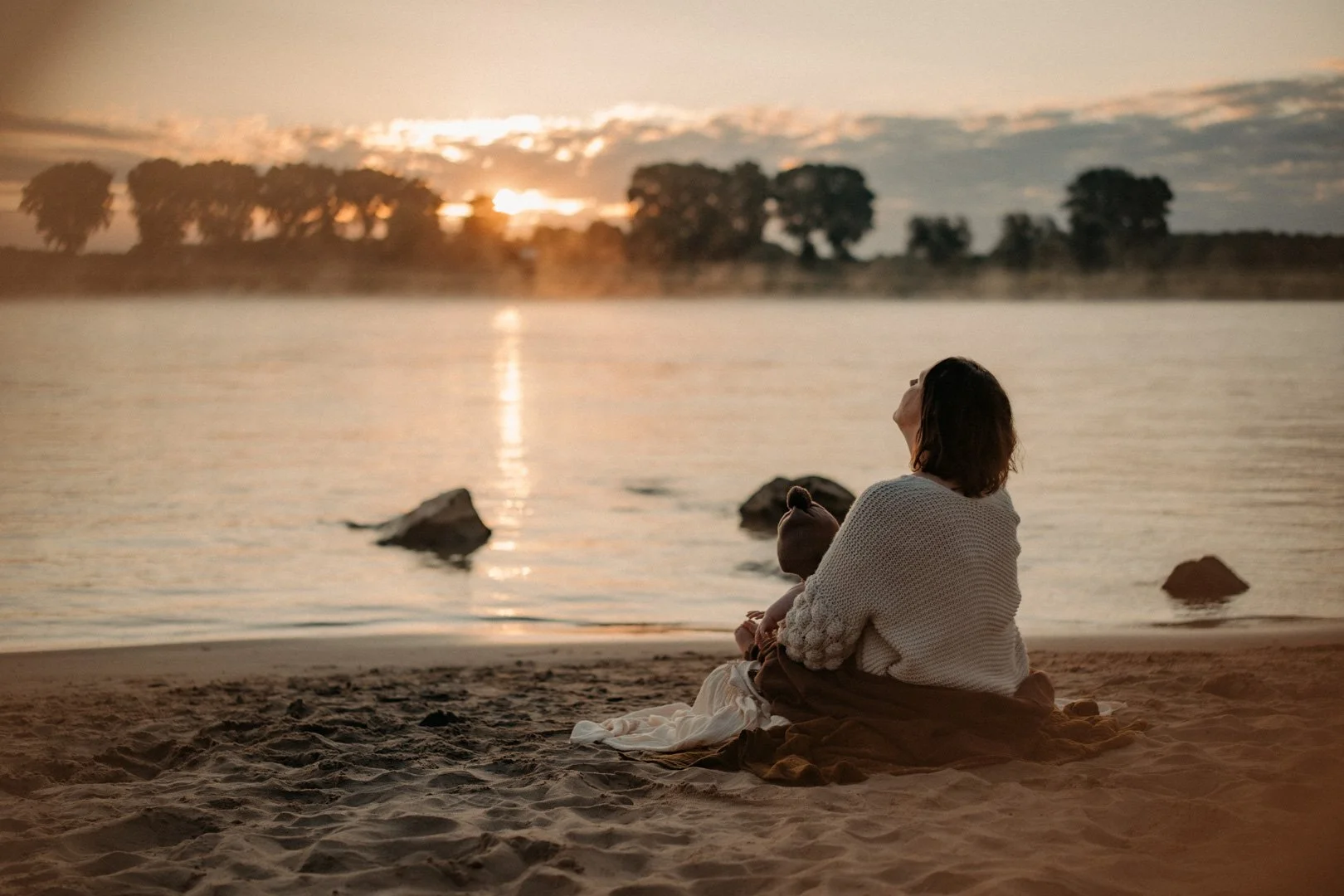 Mama und Baby kuscheln am Strand zum Sonnenaufgang