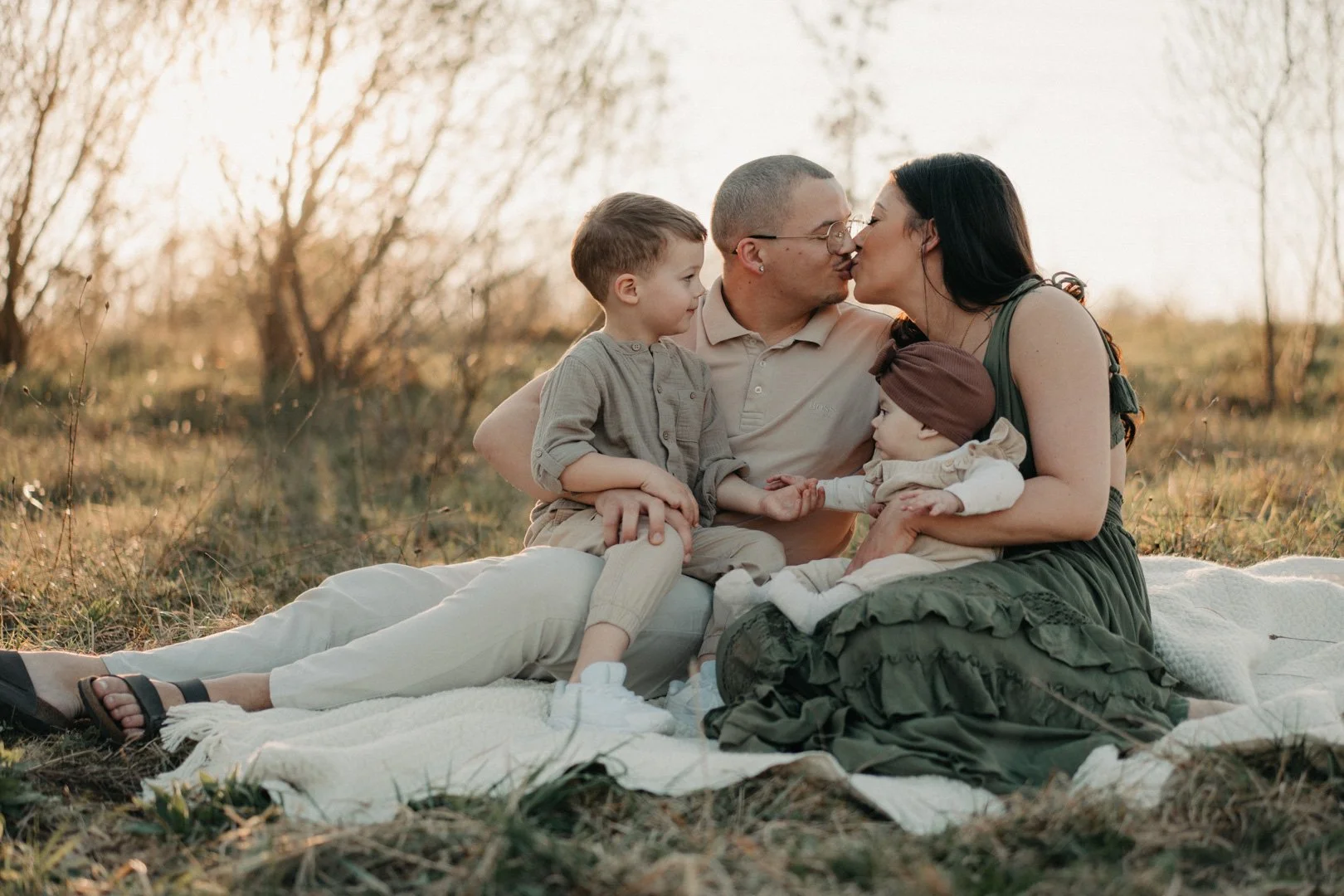 Familie sitzt zusammen auf einer Decke auf einer Wiese.