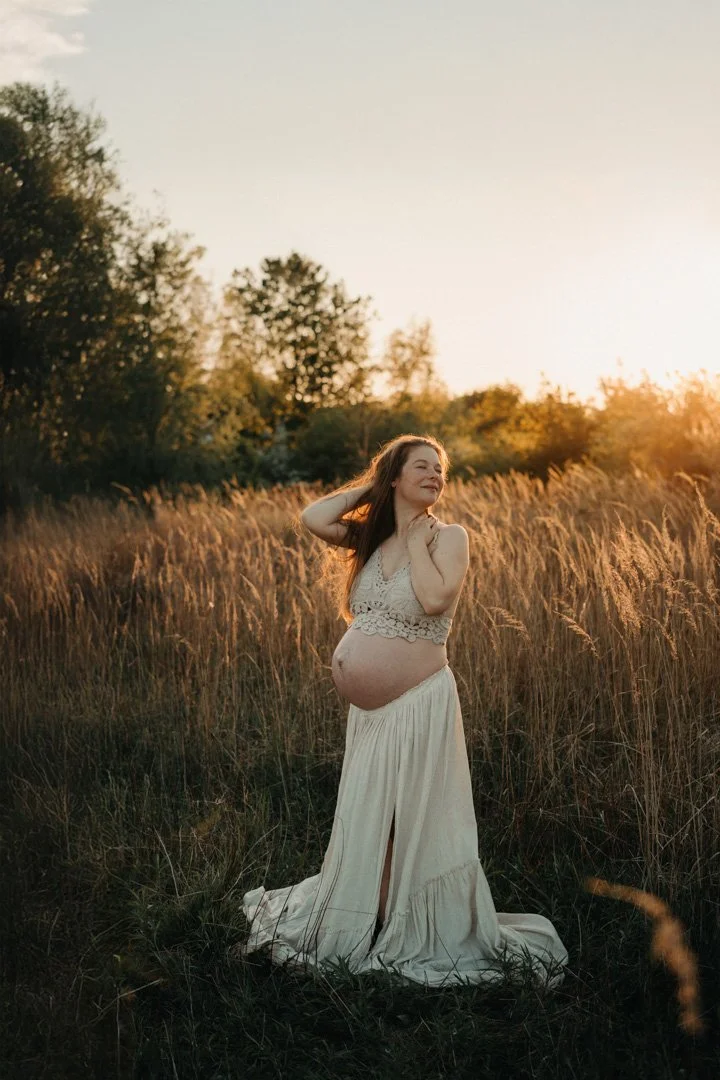Eine schwangere Mama steht in der Natur im Sonnenuntergang.
