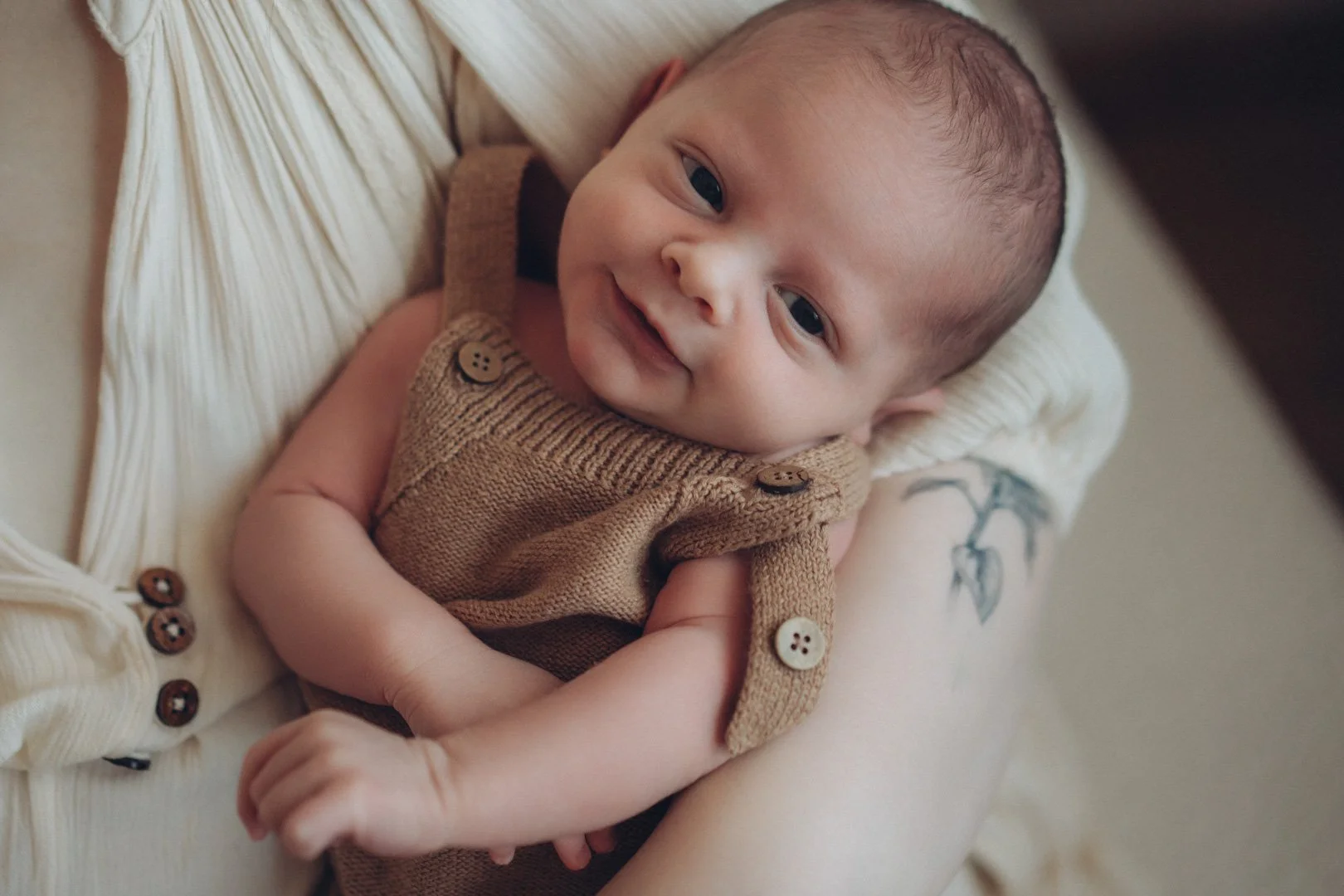 Neugeborenes Baby liegt zufrieden in Mamas Arm und lächelt.