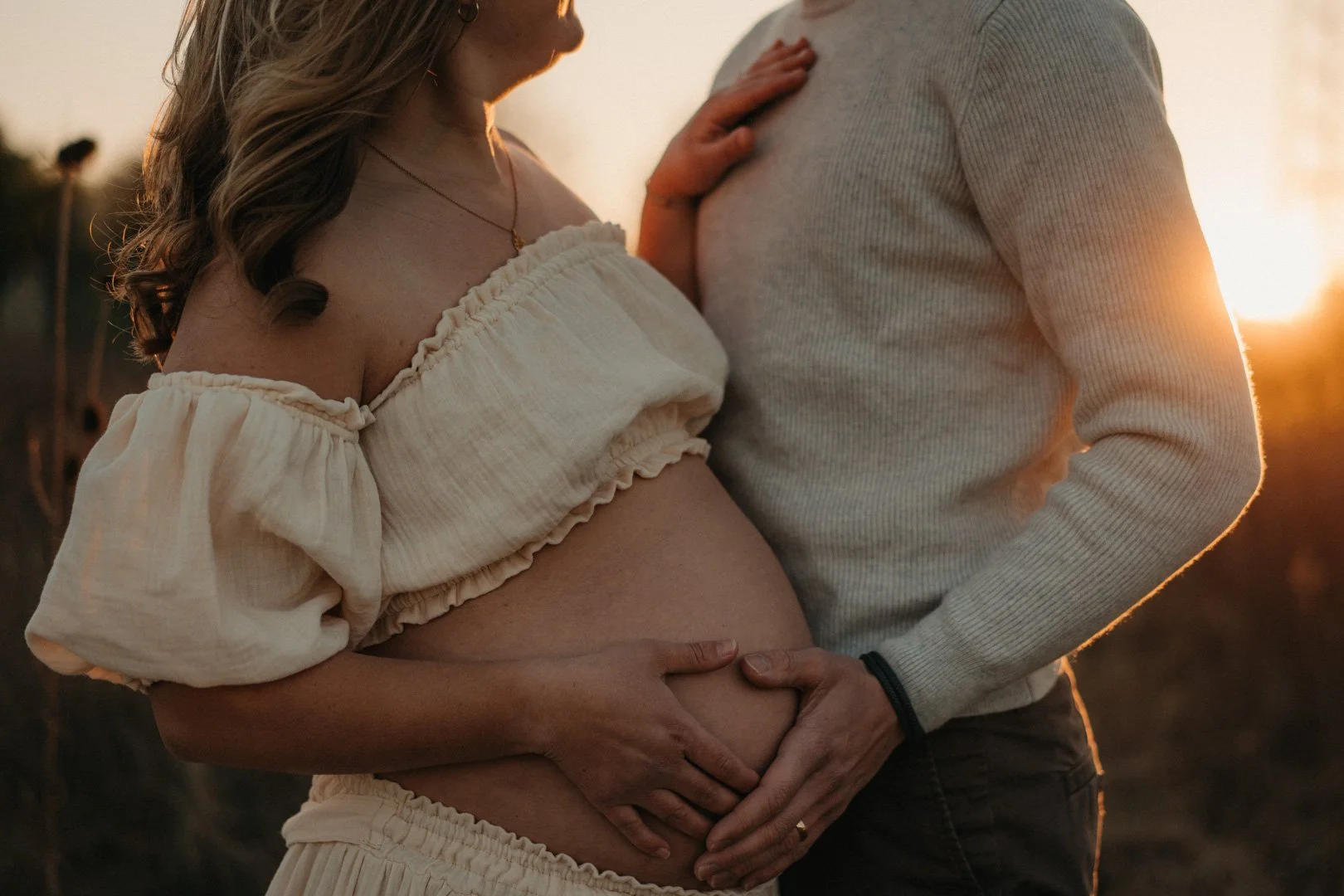 Werdende Eltern streicheln liebevoll den Babybauch im Sonnenuntergang.