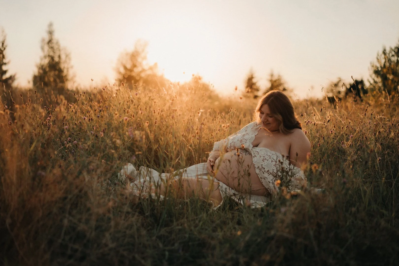 Mama sitzt im Sonnenuntergang auf einer Wiese und streichelt ihren Babybauch.
